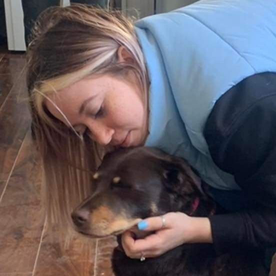 A woman in a blue vest is hugging a brown dog.