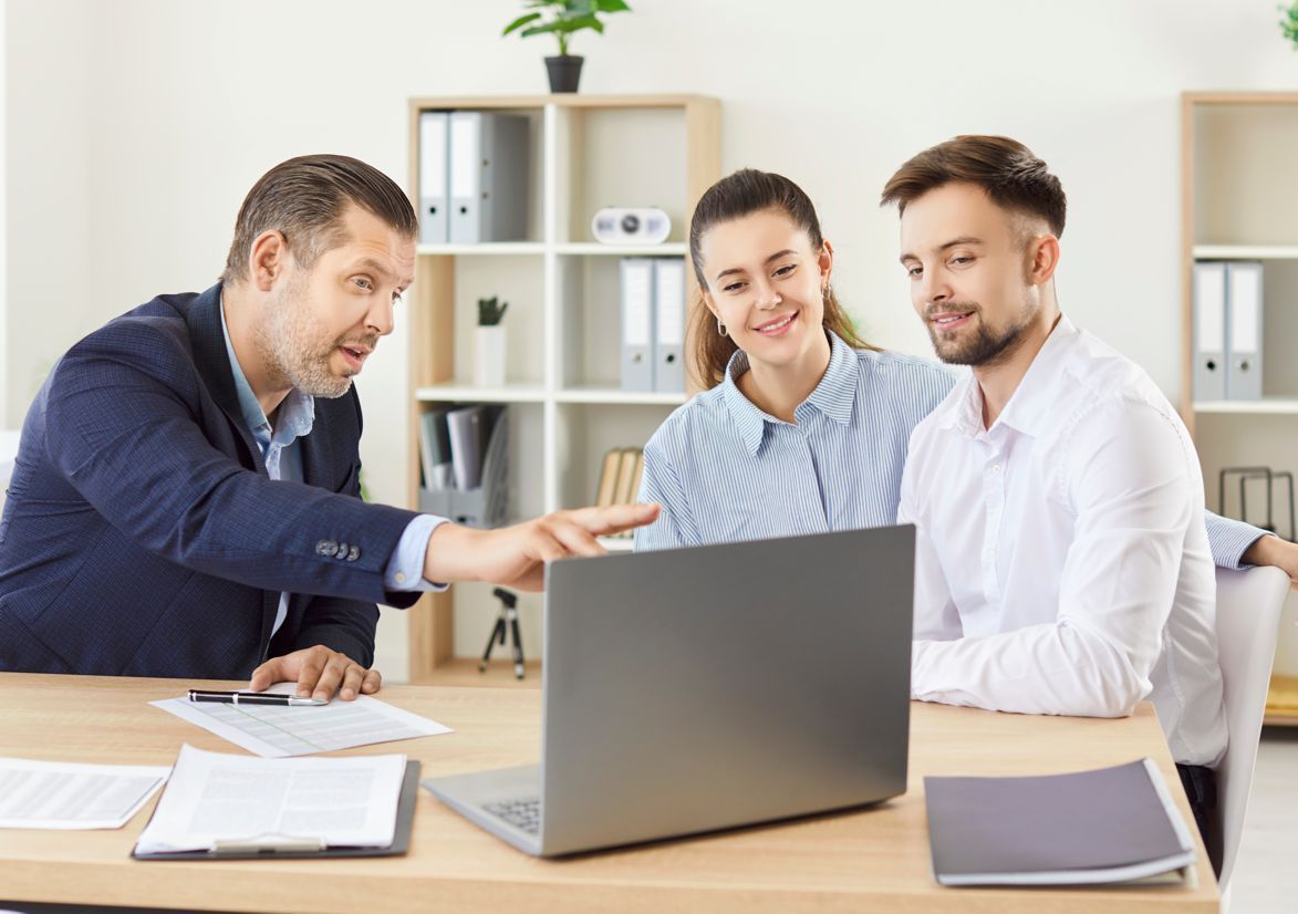 A man and a woman are sitting at a table looking at a laptop computer.