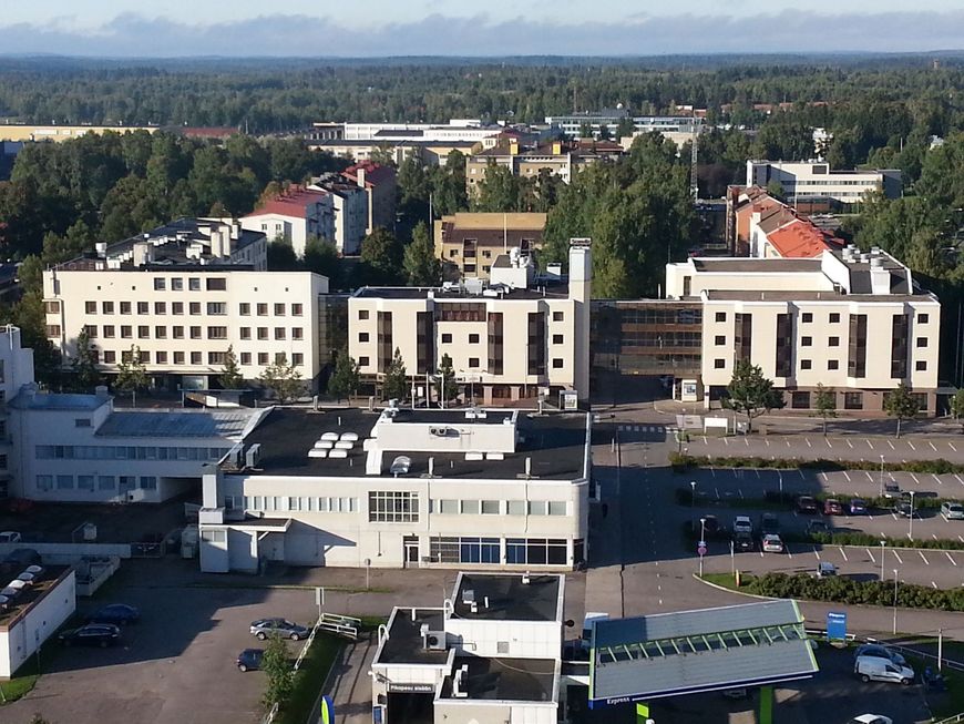 Ilmakuva suomalaisesta kaupungista, jossa on vaaleita toimistorakennuksia, päällystettyjä pysäköintialueita ja ympäröiviä vihreitä puita.