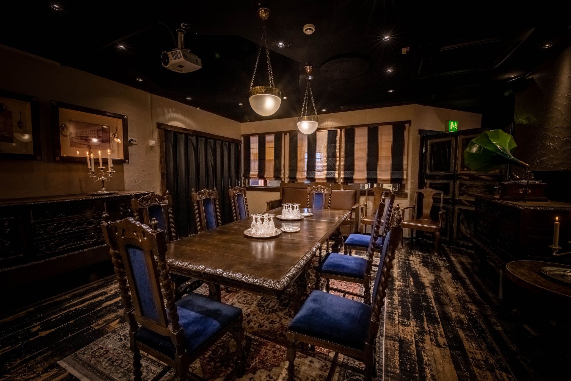 A formal dining room with a long wooden table, blue velvet chairs, and soft pendant lighting in a dim, elegant setting.