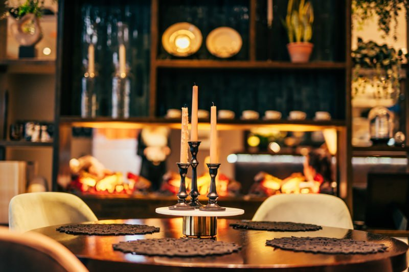 A table setting with three pillar candles in black candle holders, surrounded by dark placemats in a softly lit restaurant.