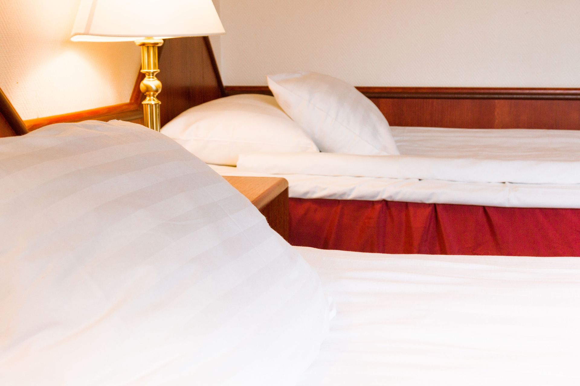 Lähikuva kahdesta hotellisängystä, joissa on valkoiset lakanat, ja lampusta puisella yöpöydällä.