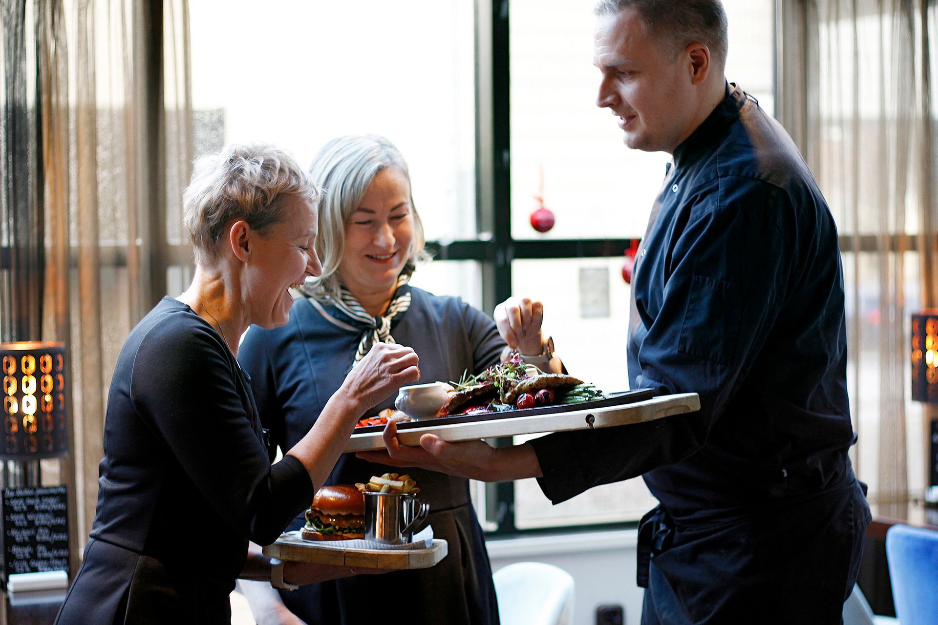 Vanhempi harmaatukkainen pariskunta seisoo lähellä toisiaan ulkoilmaympäristössä pitäen hellästi toisiaan kädestä.