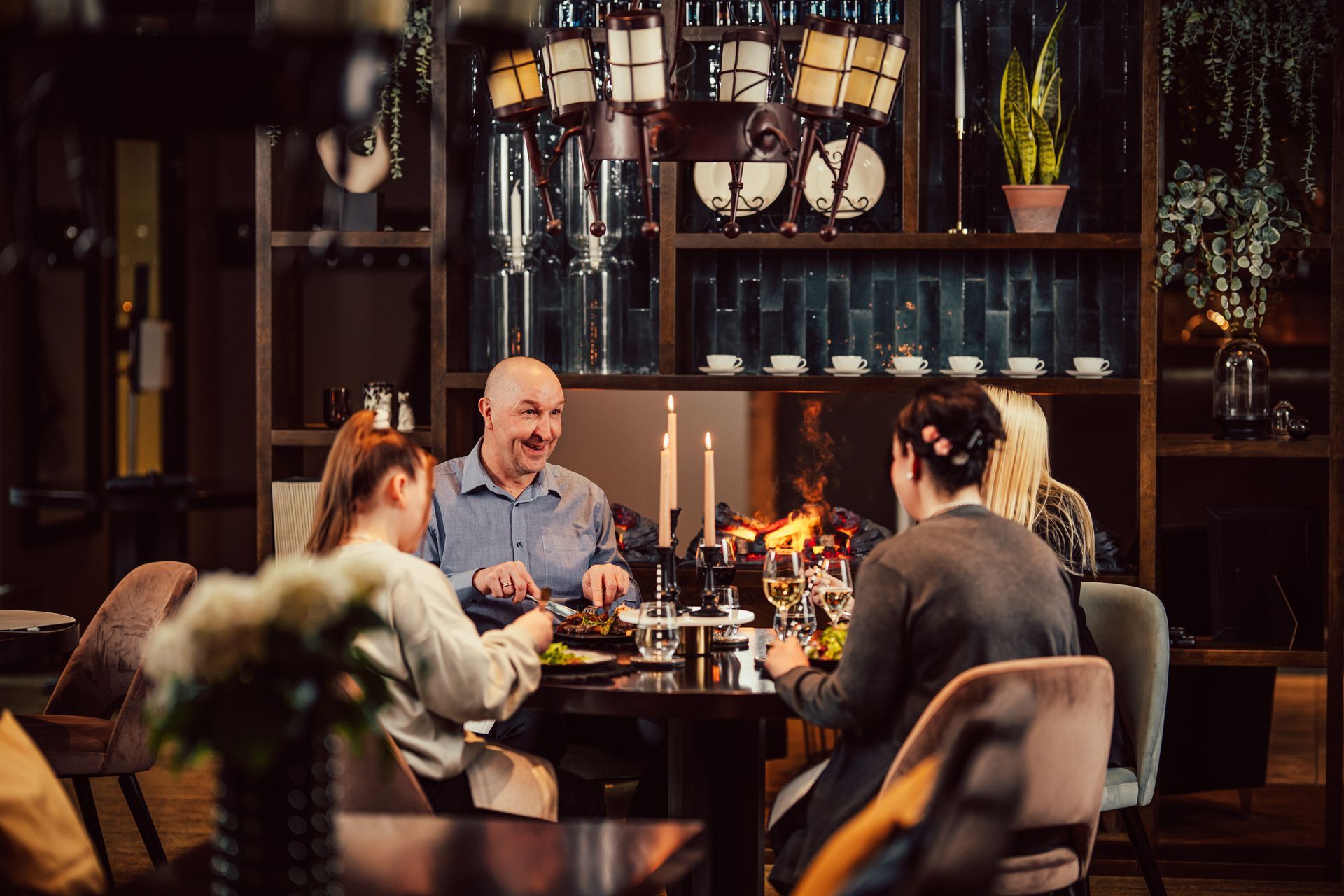 Kolme ihmistä keskustelee illallisella kynttilävalaistun pöydän ääressä viihtyisässä ja hämärässä ravintolassa.