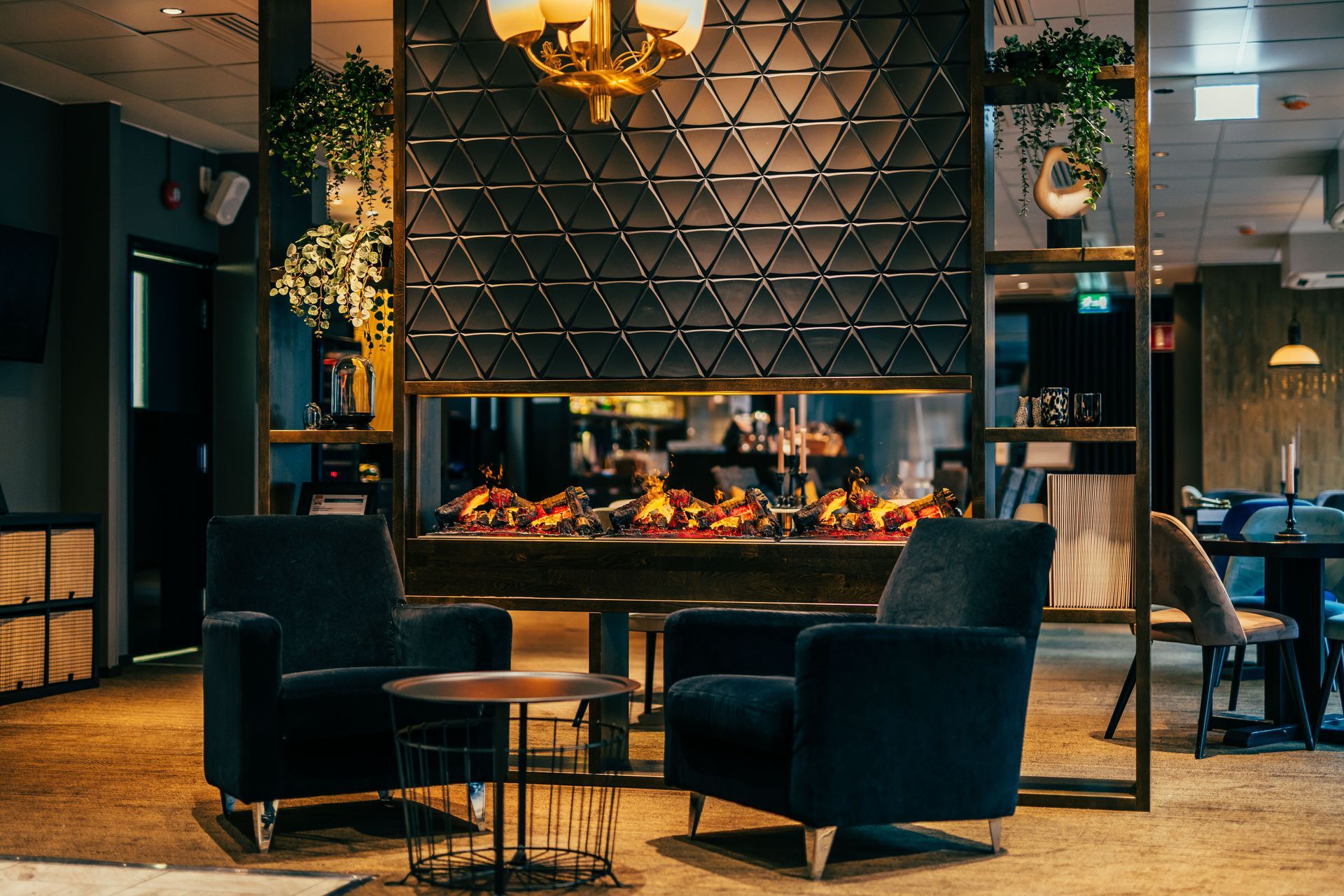 Kaksi tummaa nojatuolia on modernin, geometrisella mustalla sermillä varustetun takan edessä viihtyisässä, hämärästi valaistussa oleskelutilassa.