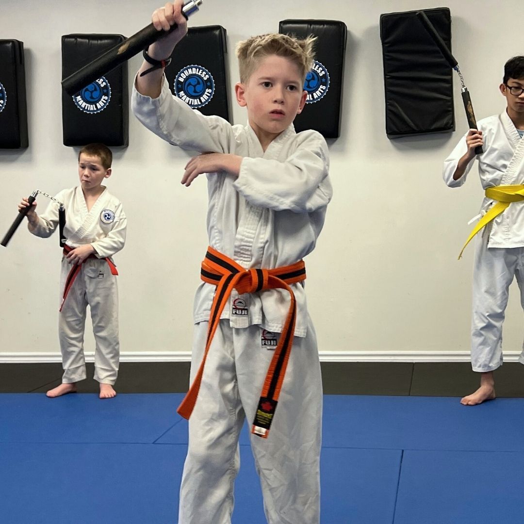 Two people grappling on a mat, one in a black gi, the other in a rash guard, legs entangled.