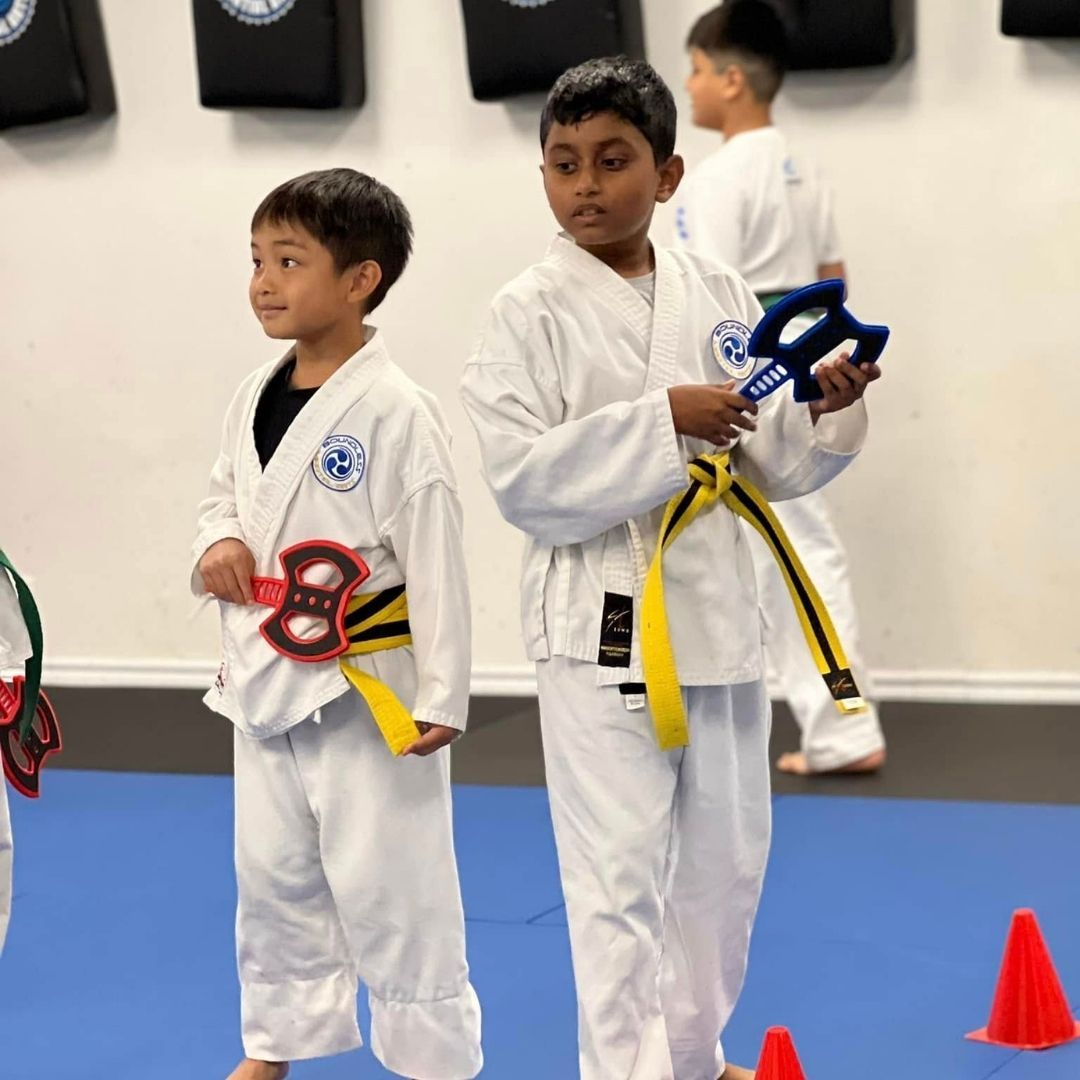 Two boys on a mat practicing Jiu-Jitsu. One boy is on top, giving a thumbs-up.