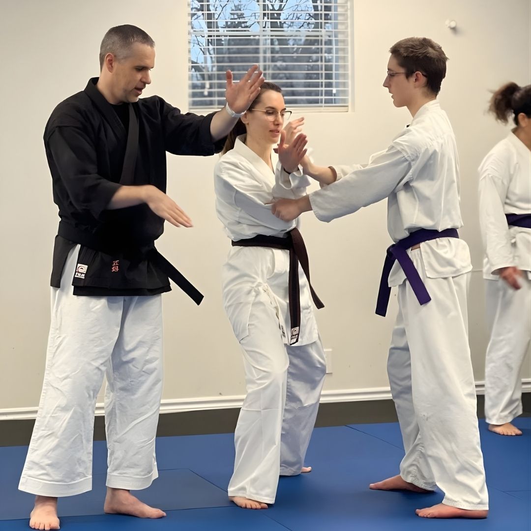 Two people practicing Brazilian Jiu-Jitsu on a mat; one in a black gi, one in a white gi, grappling.