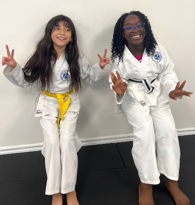 Family in Jiu-Jitsu gis poses. Indoors, blue mats, a smiling woman in the middle, around a seated man with a beard.