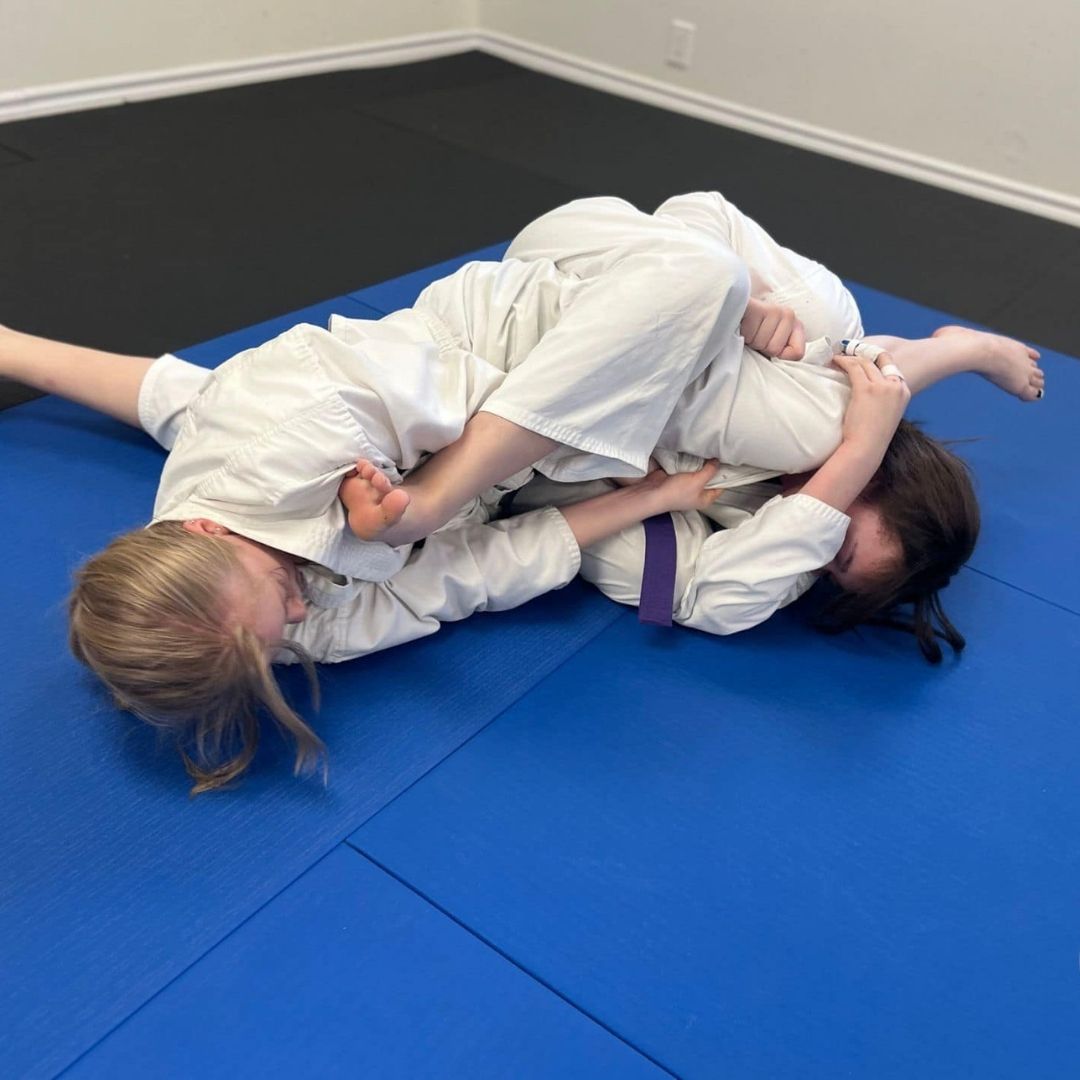 Two children grappling on a mat, one in a headlock.