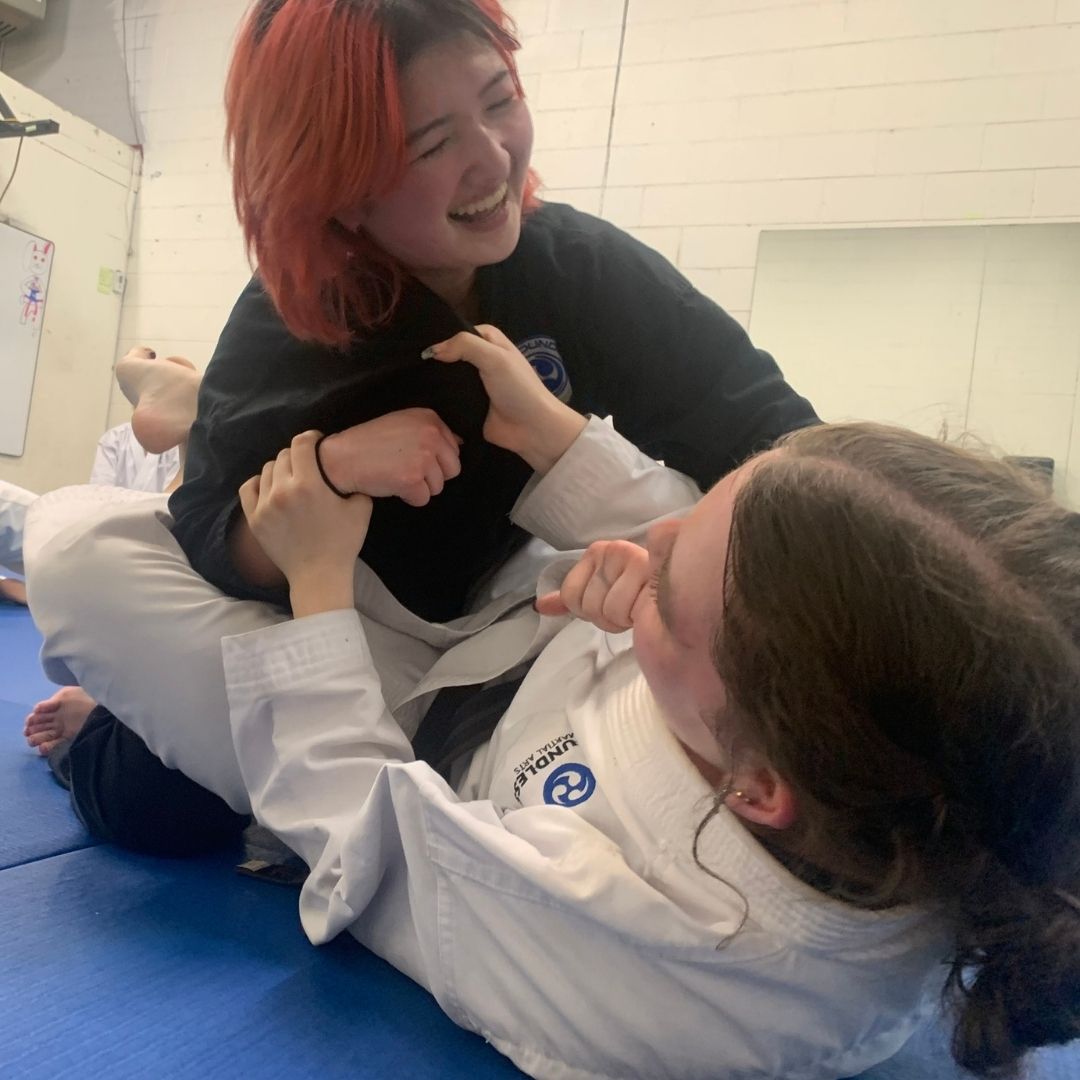 Two people practicing Brazilian Jiu-Jitsu on a mat. One is on top, applying a hold.