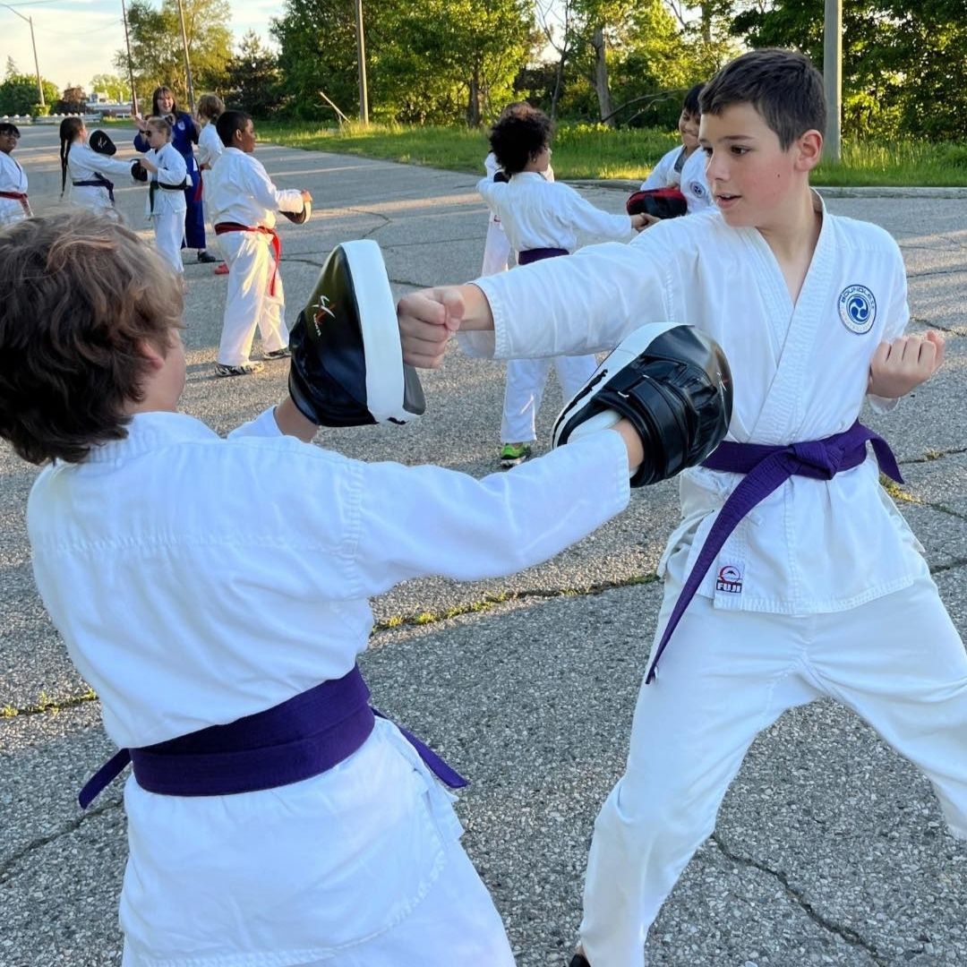 Group of children in martial arts attire posing, some with arms around each other, in a gym.