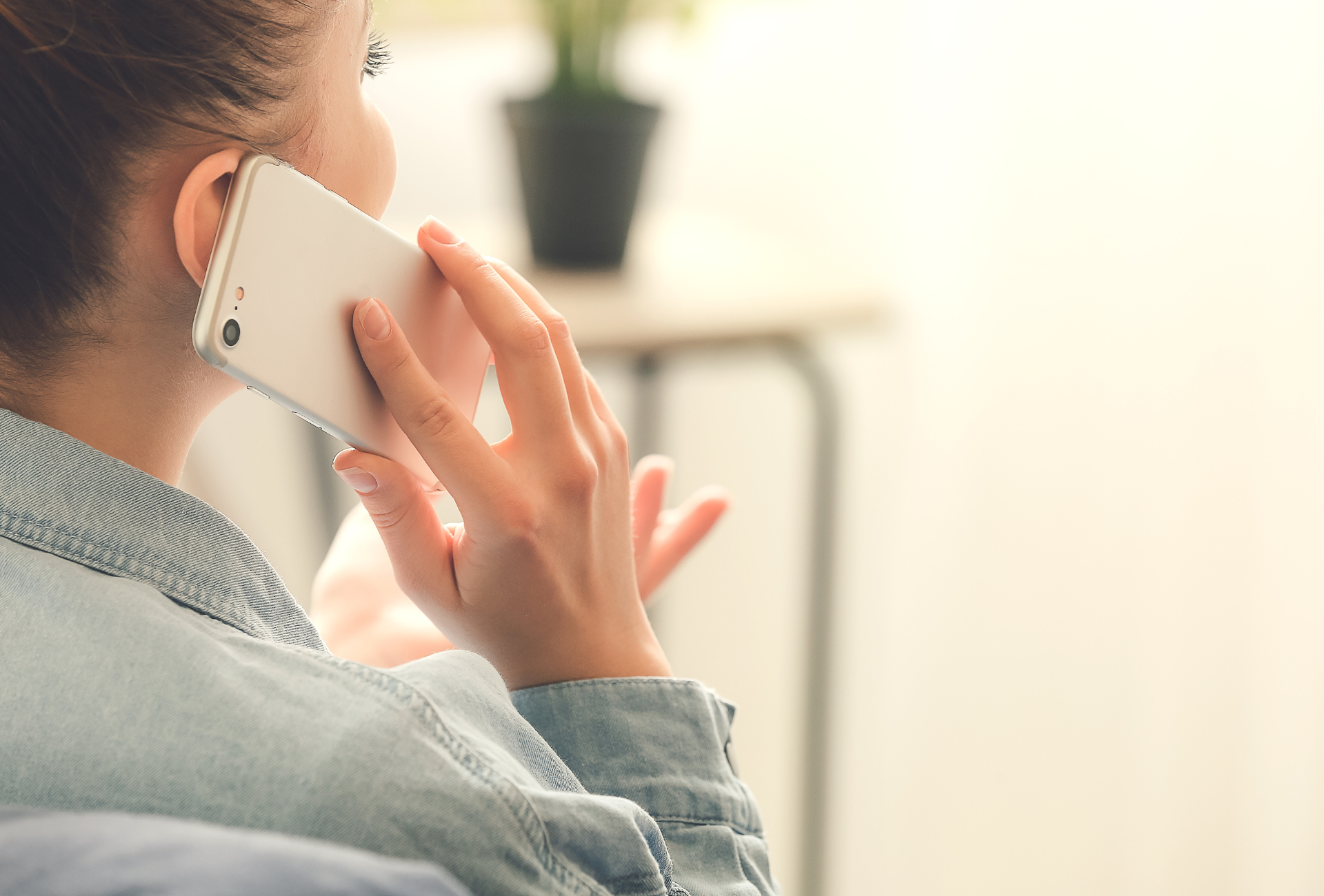 Woman in denim shirt holding a white smartphone to her ear.