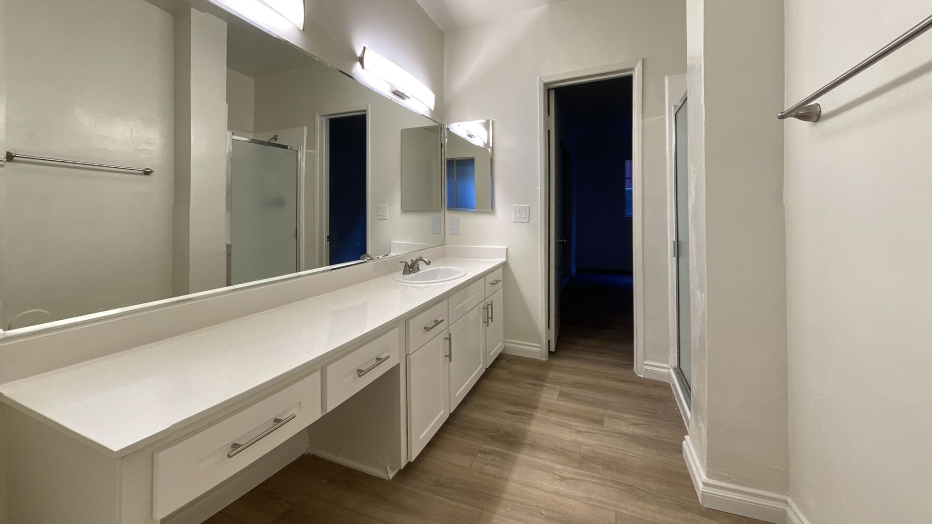 Bathroom with white cabinets, long countertop, large mirror, and open doorway.