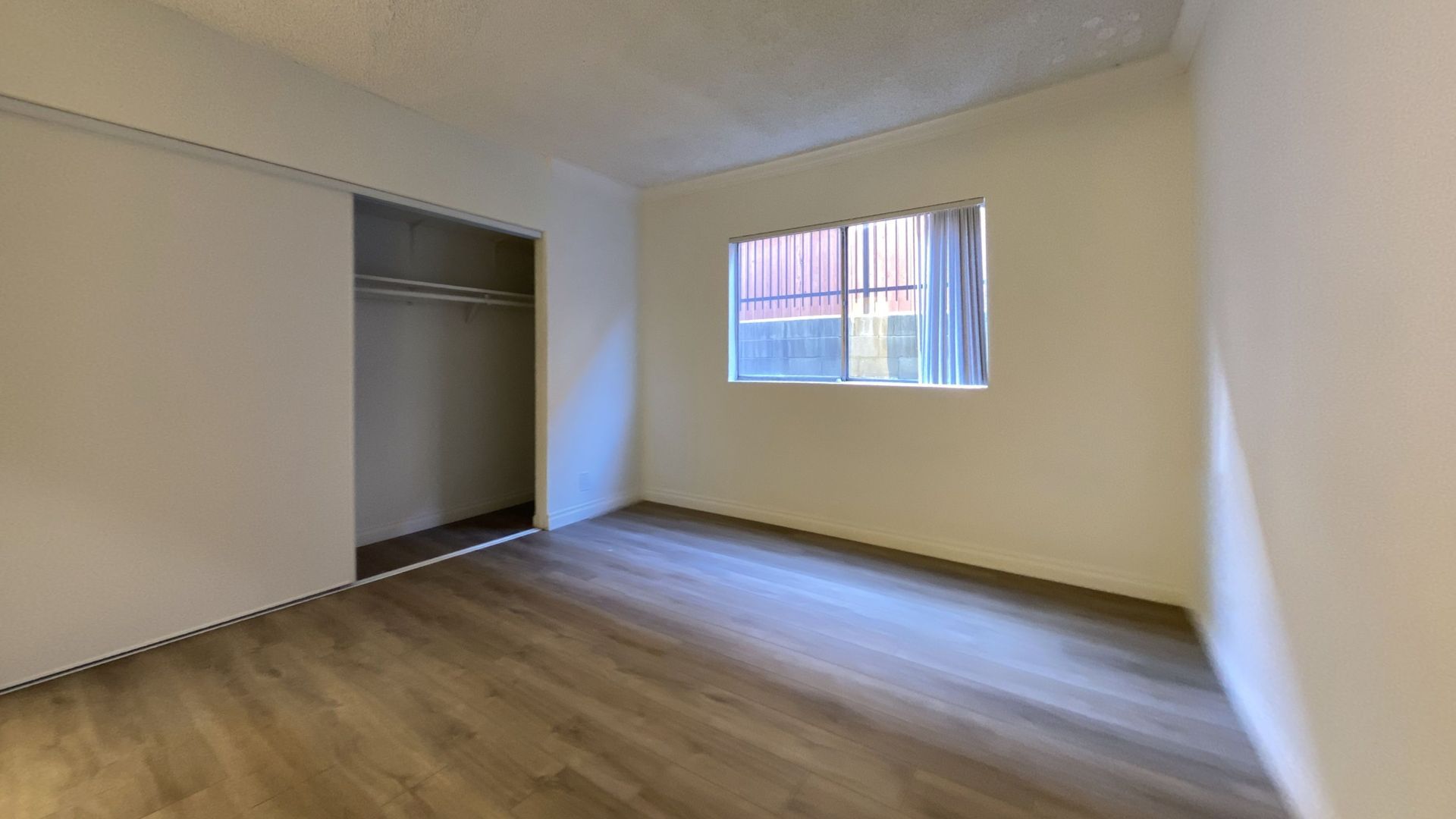 Empty room with wood floors, closet, window with bars, and white walls.