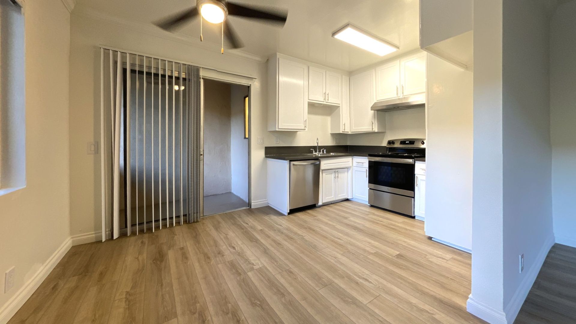 Kitchen with stainless steel appliances, white cabinets, and wood-look flooring, connected to an entryway.