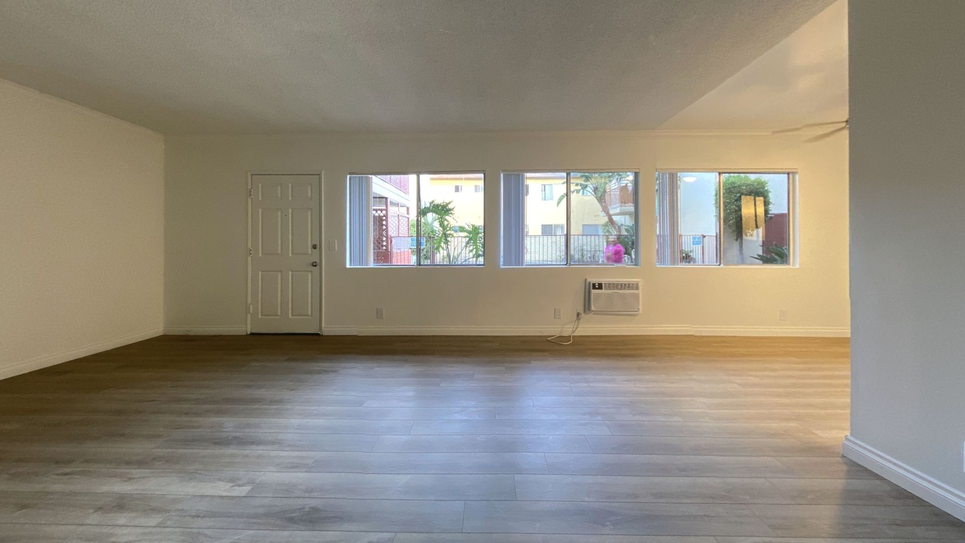 Empty living room with wood flooring, white walls, windows, and a door.