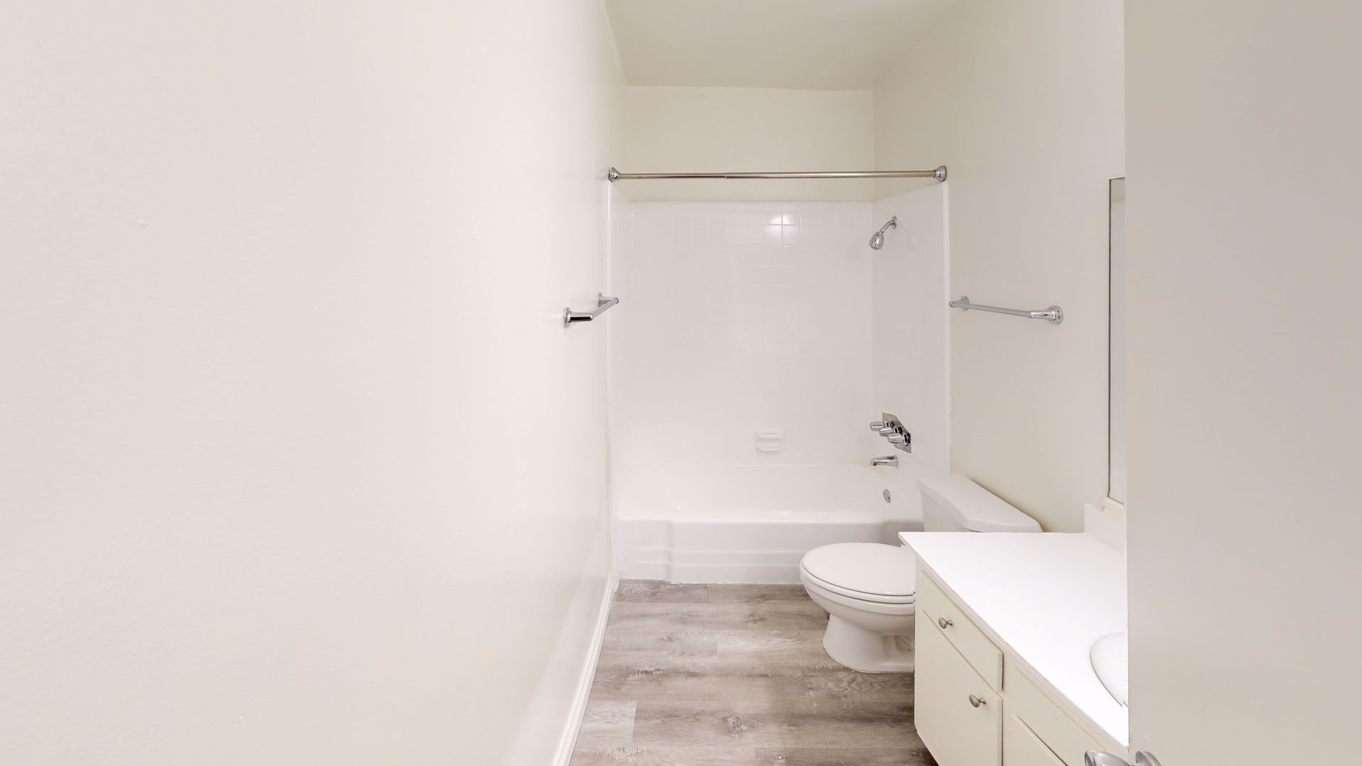 White bathroom with a bathtub, toilet, vanity, and gray wood-look flooring.