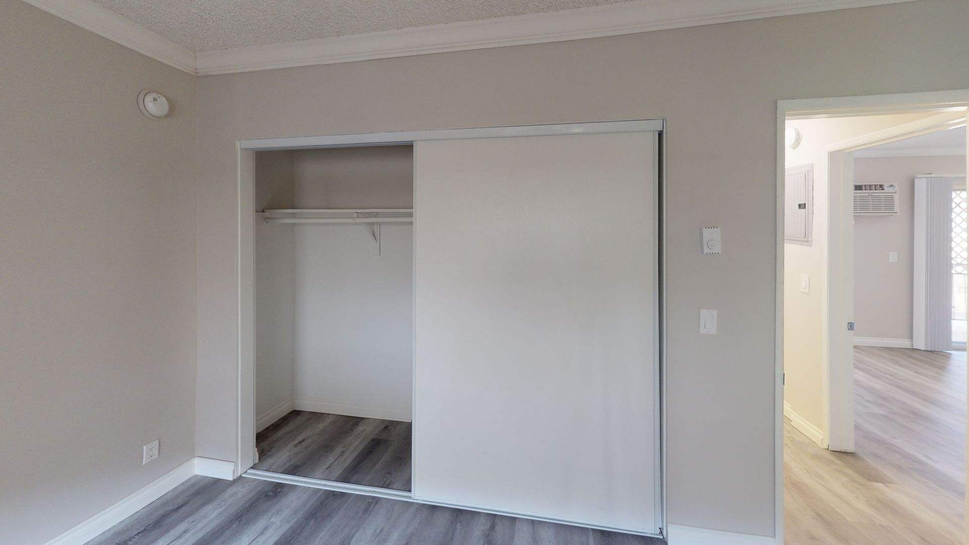 Empty closet with sliding door in a room with light gray walls and wood-look flooring.