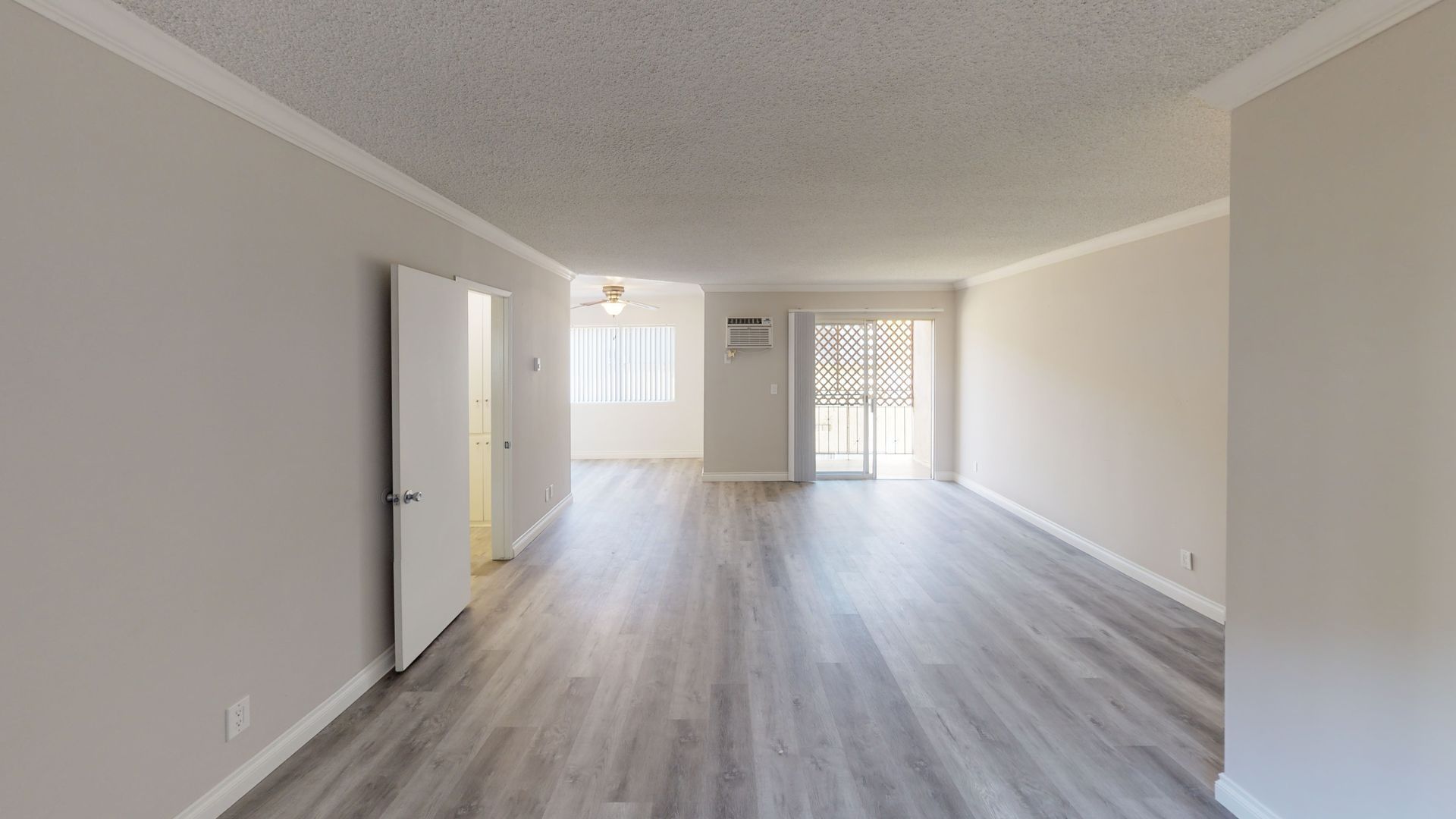 Empty apartment interior with gray flooring, light walls, and a sliding glass door.