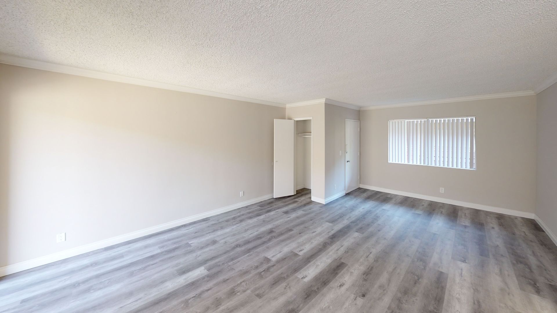 Empty room with gray laminate flooring, white walls, closet, window with blinds.