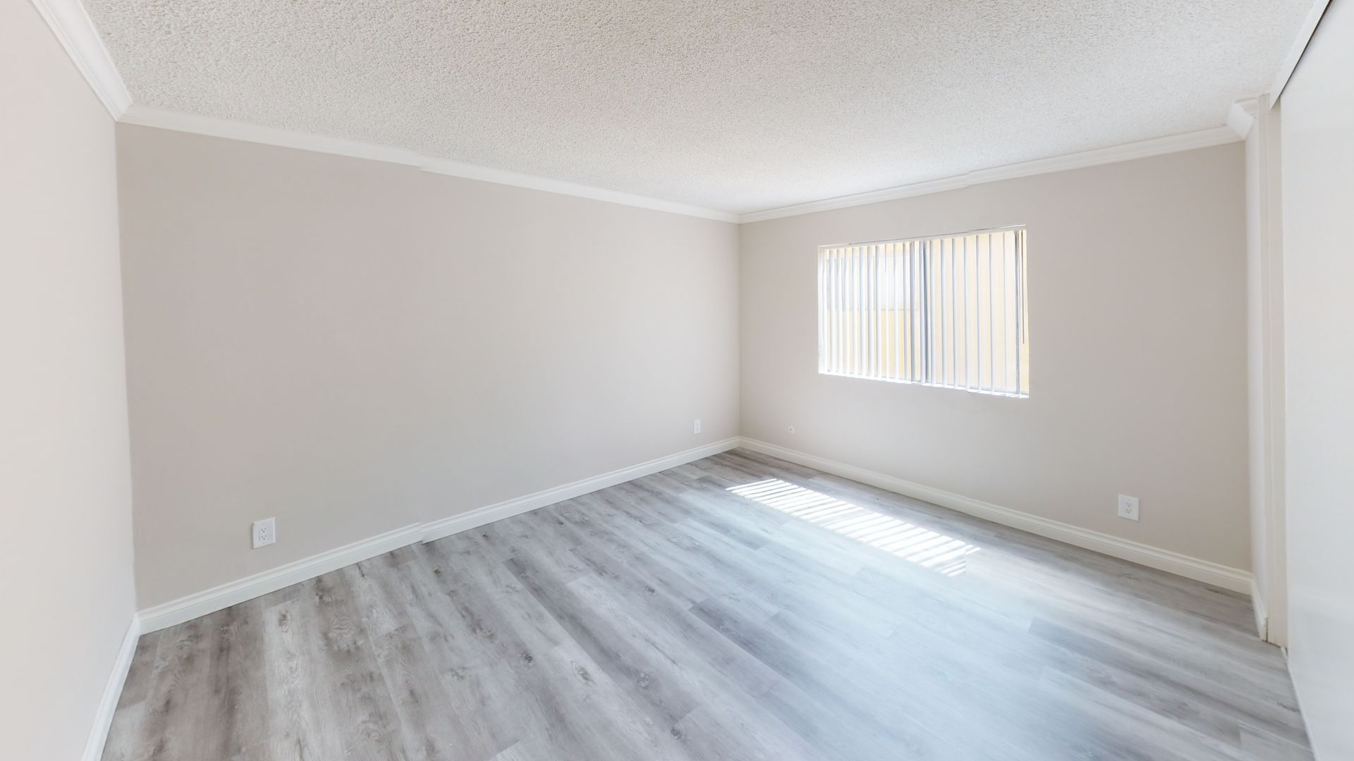 Empty room with gray wood-look flooring, light gray walls, and a window with blinds.