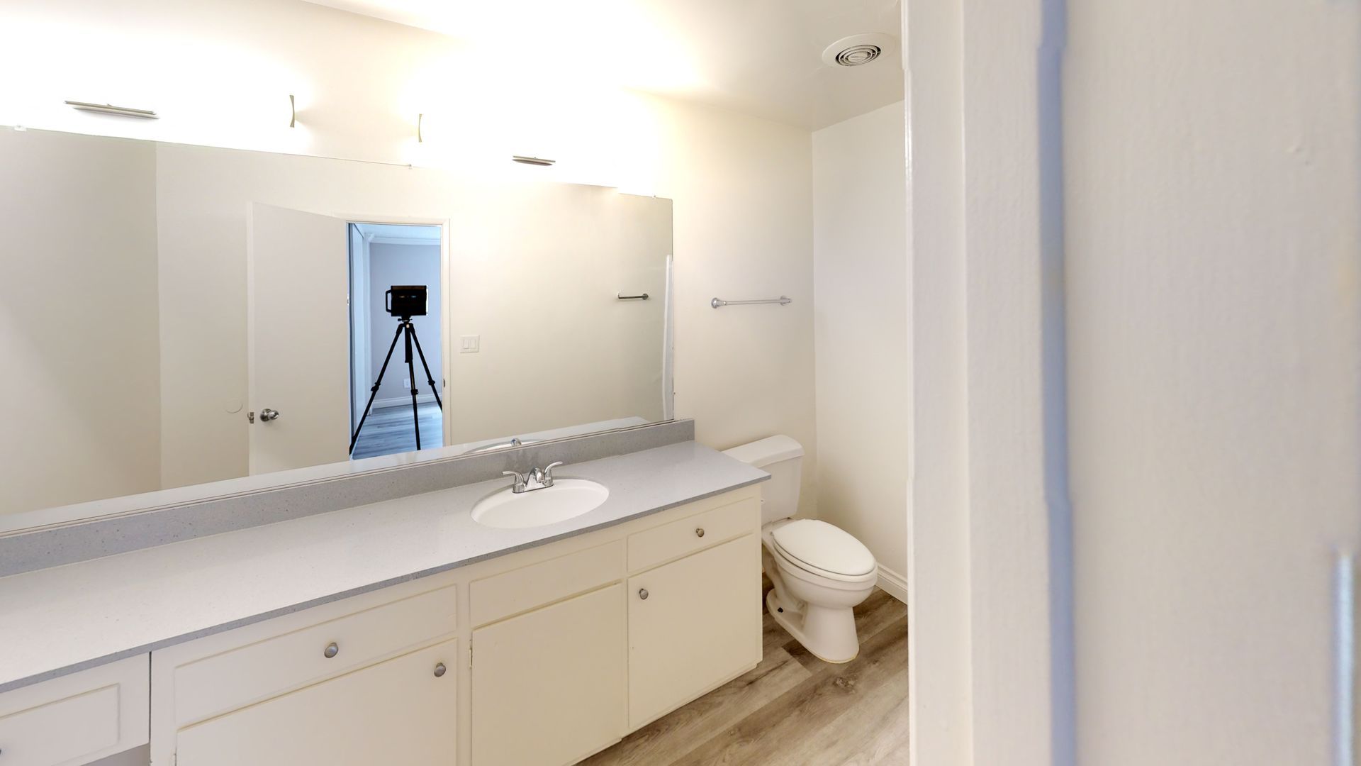 Bathroom with large mirror, vanity, toilet, and a tripod in the doorway.