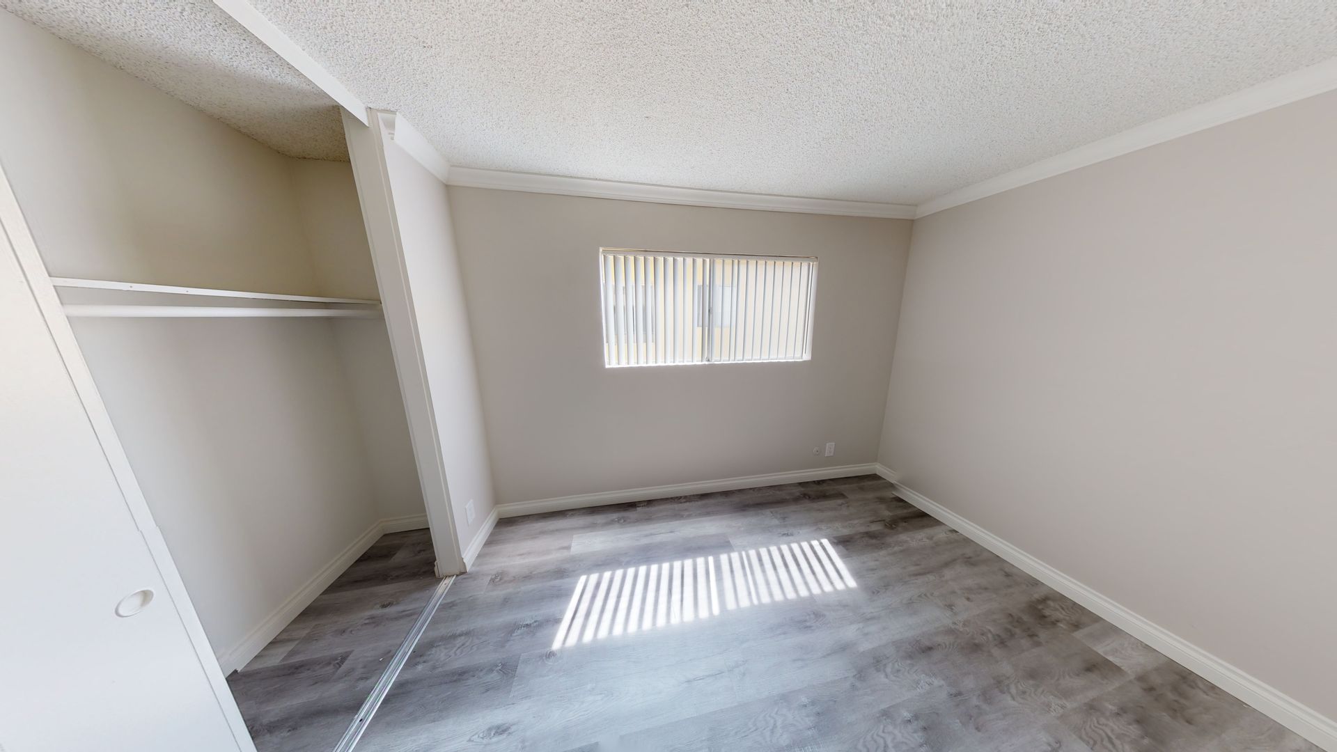 Empty room with closet and window, gray laminate flooring, white walls and ceiling.