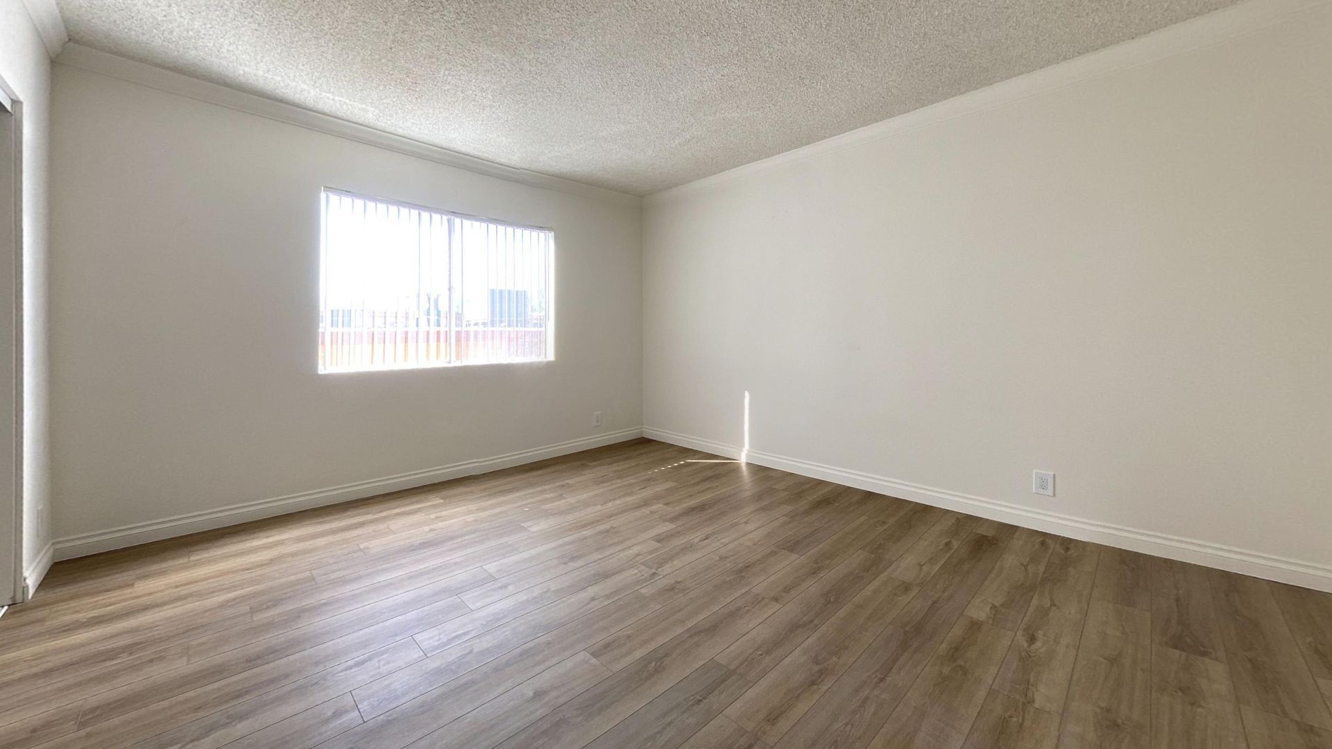 Empty room with wood-look flooring, white walls, and a window with blinds.