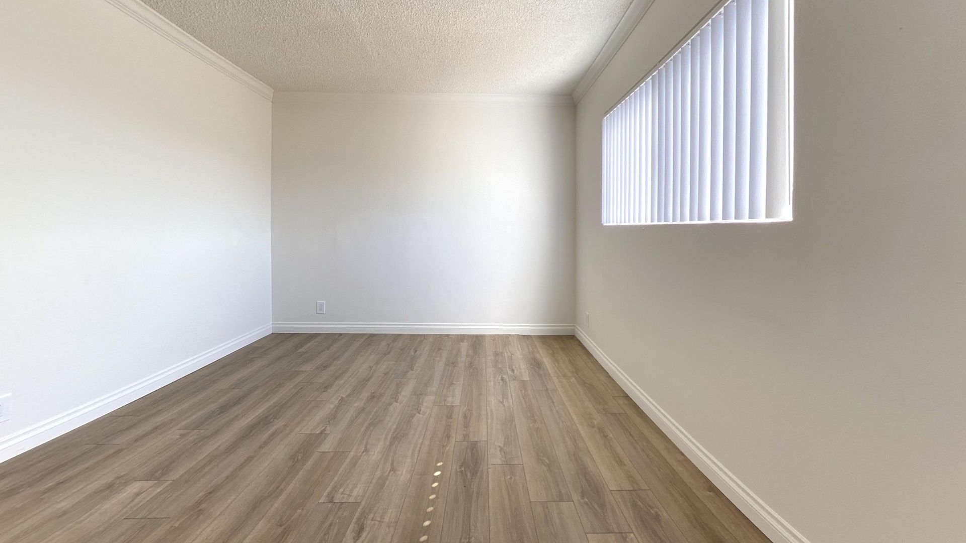 Empty room with wood-look flooring, white walls, and a window with blinds.