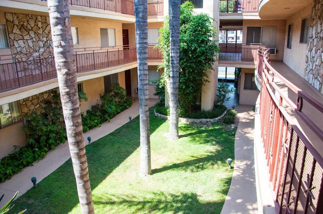 Courtyard of a two-story apartment building with palm trees, grass, and walkways.