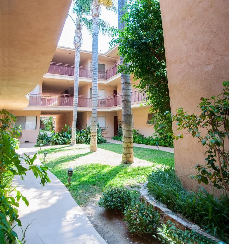 Courtyard with three-story apartment building, palm trees, and landscaping.