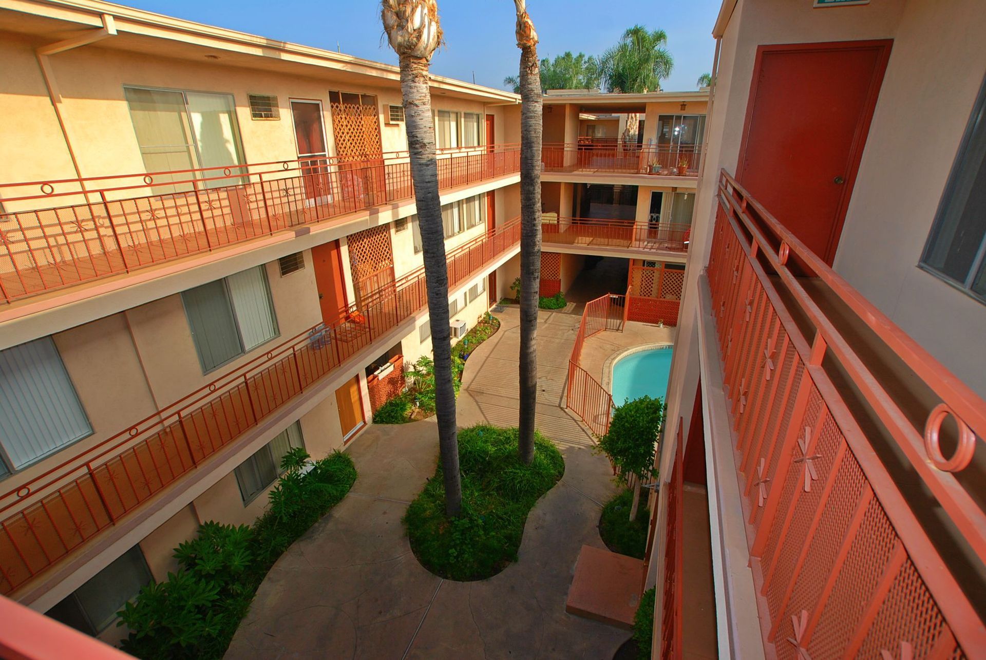 Apartment complex with red balconies, palm trees, and a pool in a courtyard.