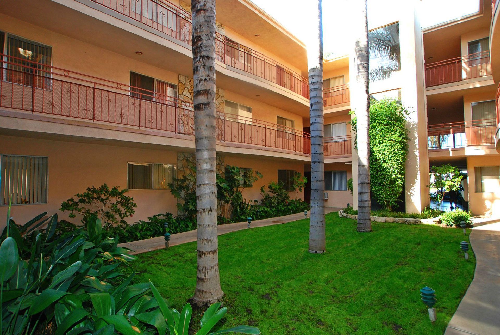 Courtyard with tan apartment building and palm trees. Green lawn and shrubbery.