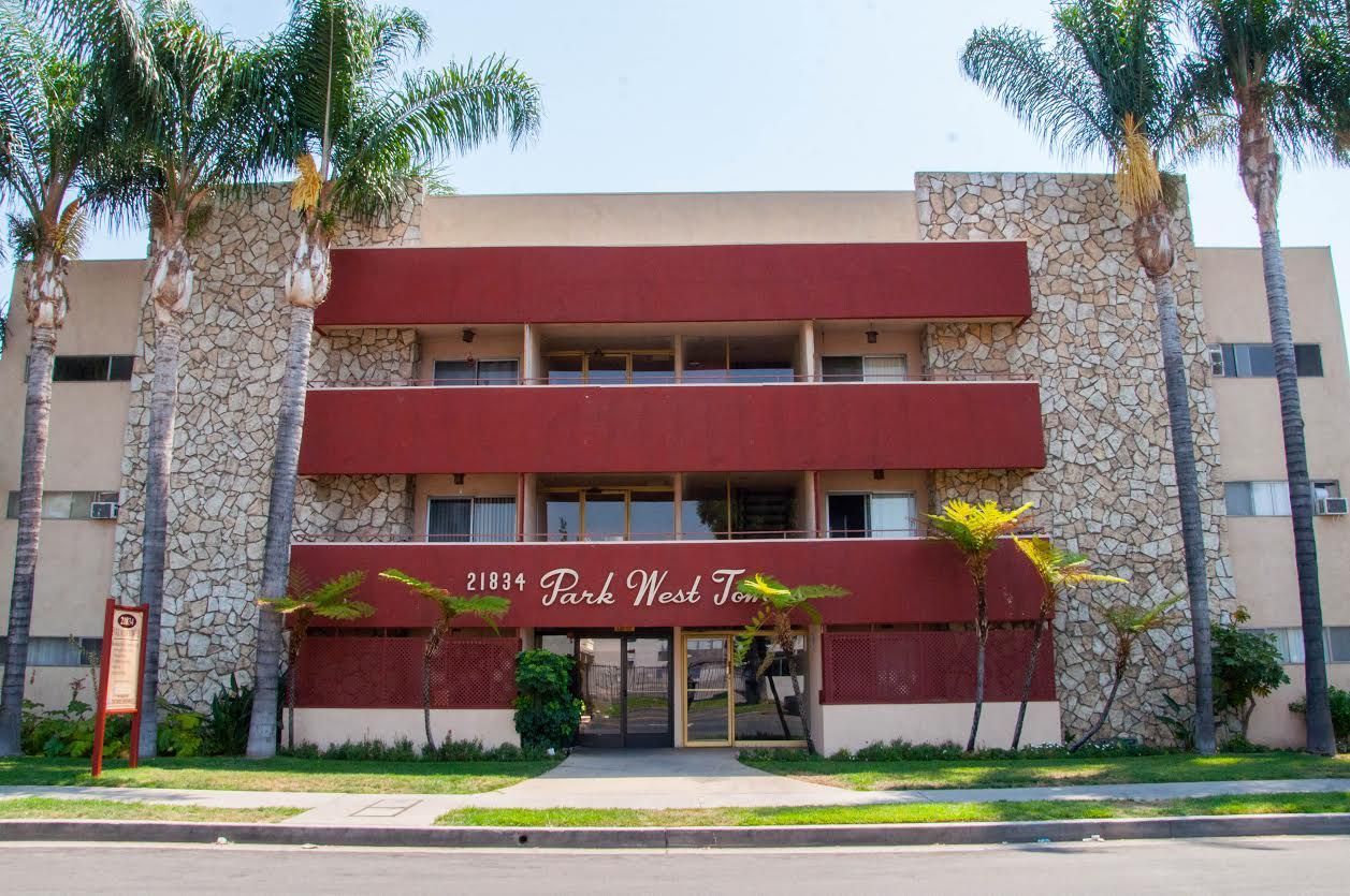Three-story apartment building with red accents, stone facade, and palm trees in front.