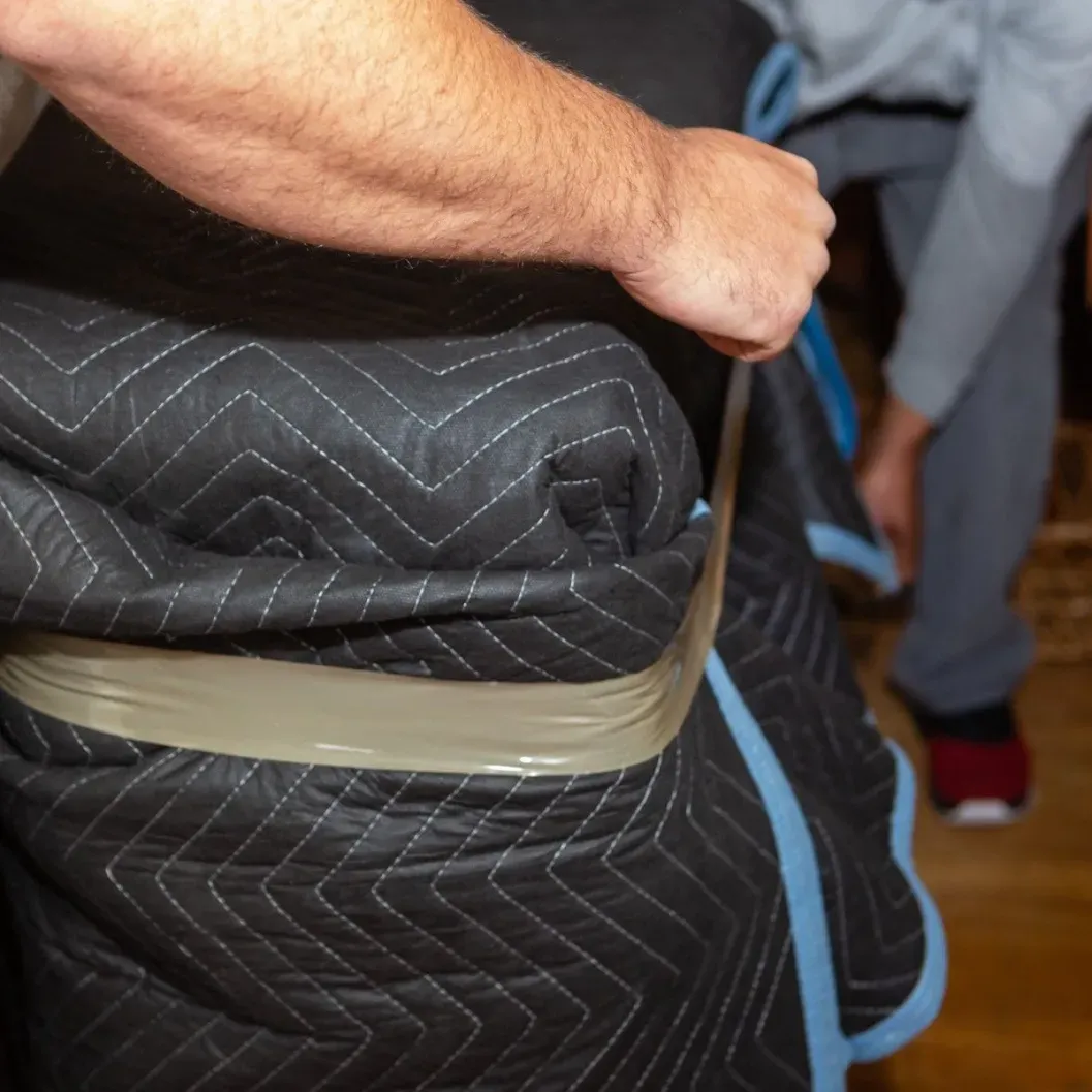 Person wrapping a piece of furniture in a quilted moving blanket and securing it with tape.