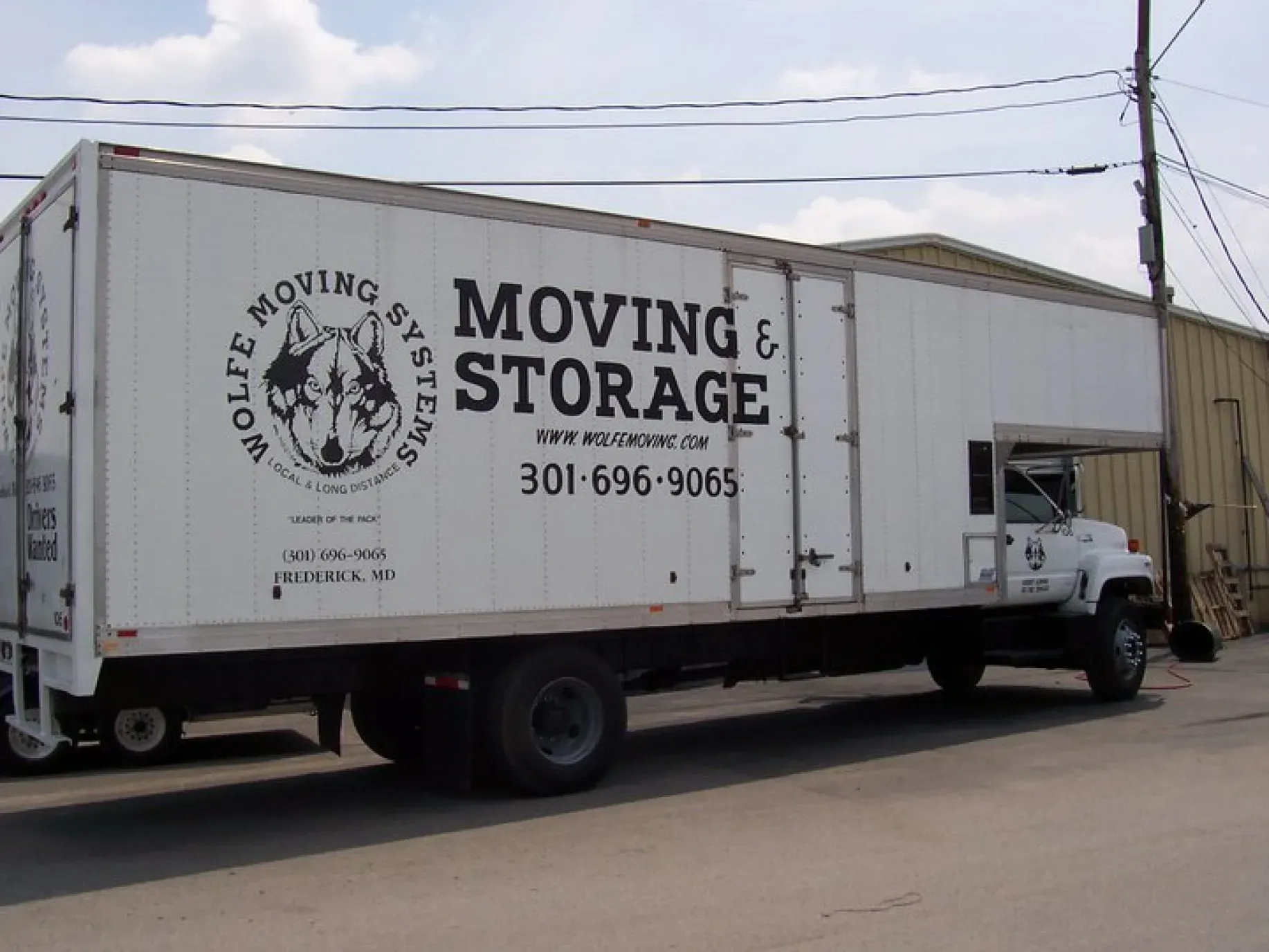 White Wolf Moving & Storage truck parked on a paved road. The truck is white with black lettering and a wolf logo.