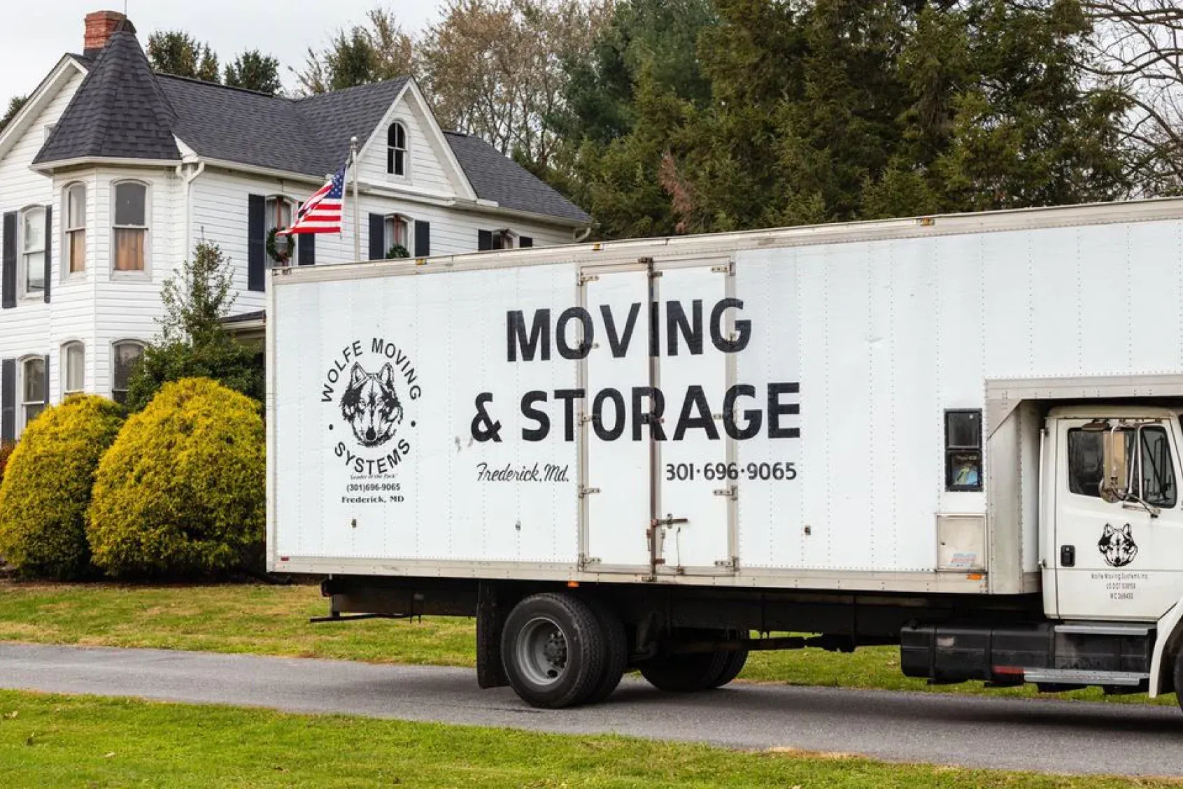 Moving truck parked in front of a white house with an American flag.