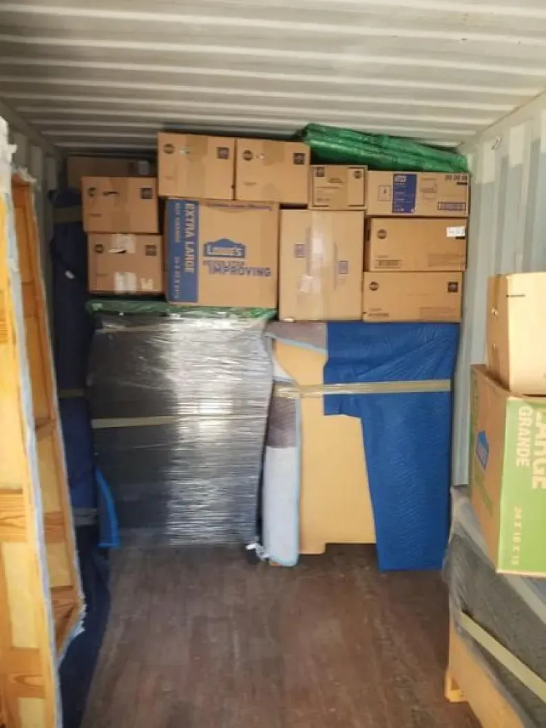 Interior of a storage container packed with moving boxes and wrapped furniture.