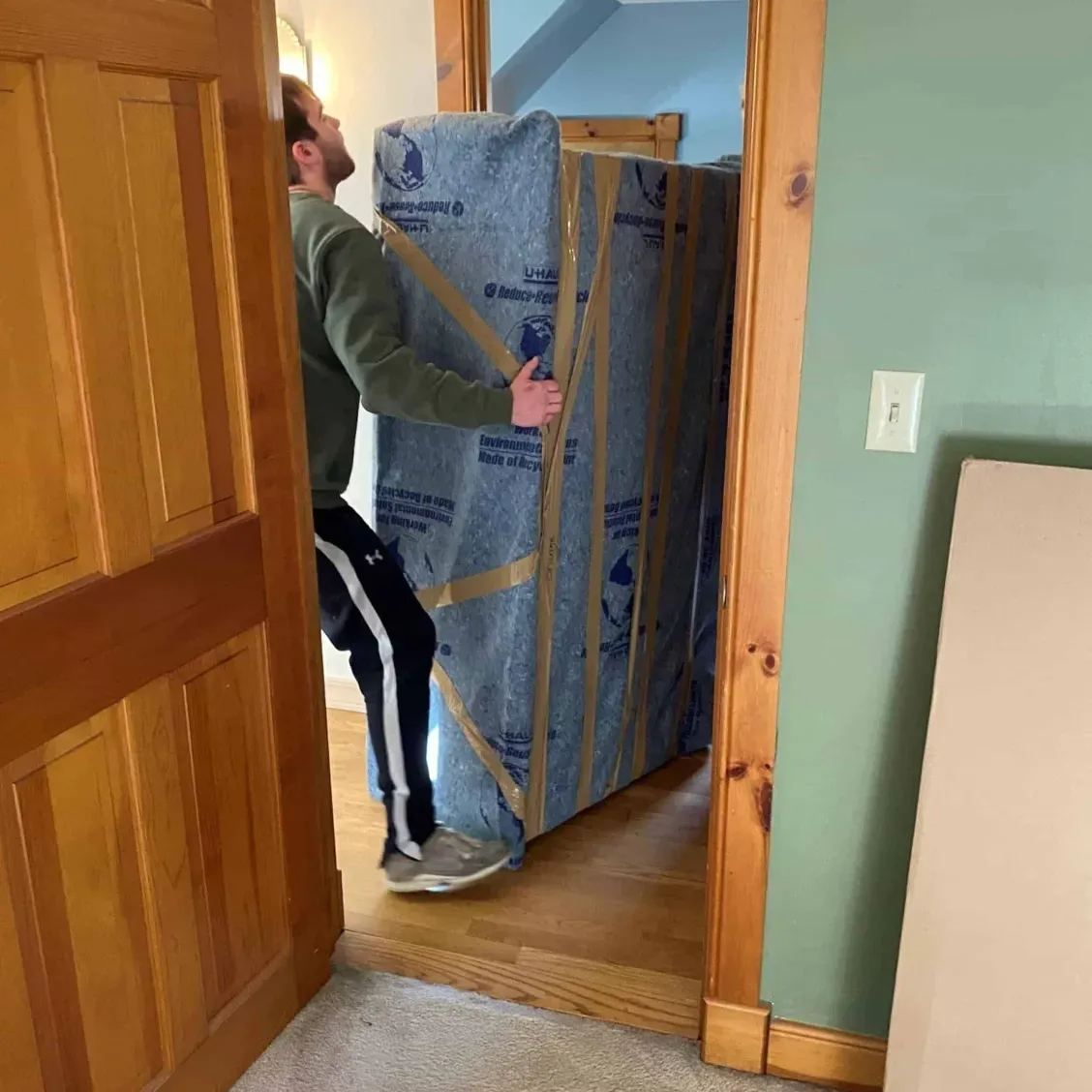 Man carrying a large, wrapped rectangular item through a doorway.