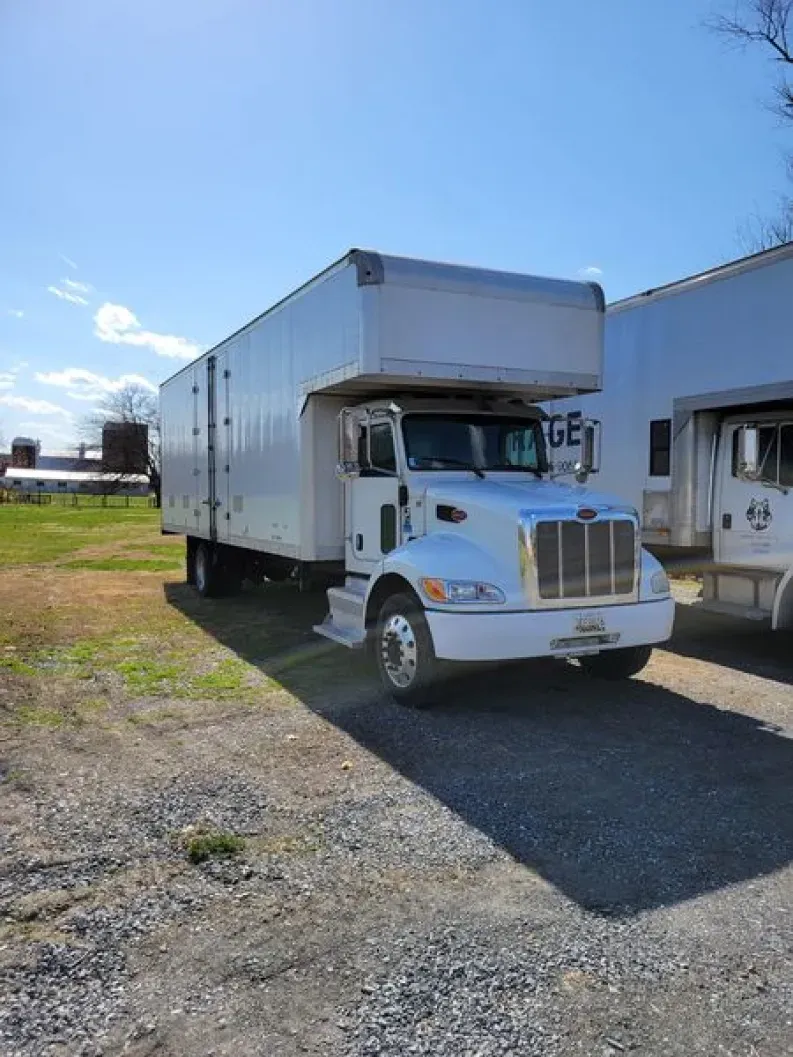 White box truck parked on gravel and grass. Sunny day. Another truck visible to the right.