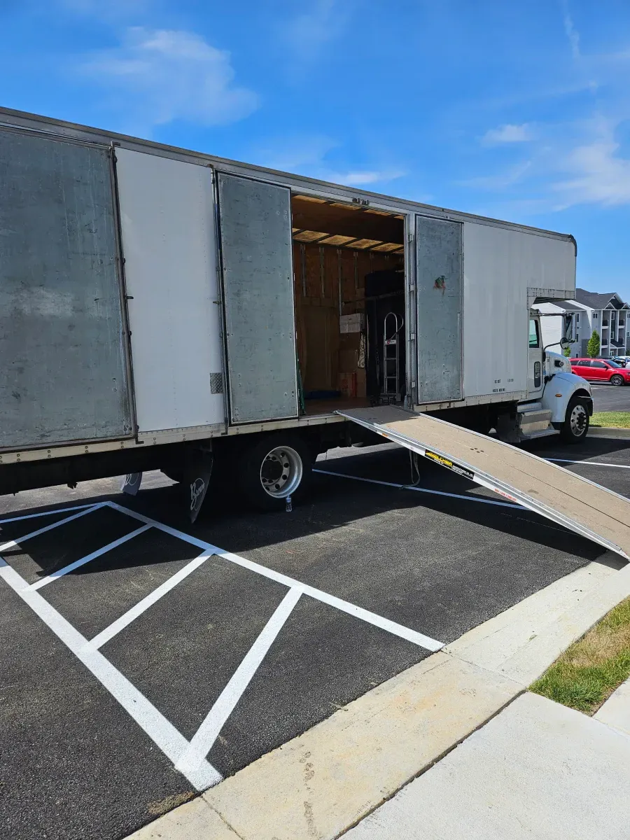 White moving truck with ramp extended, parked in a parking space. Open doors reveal inside.