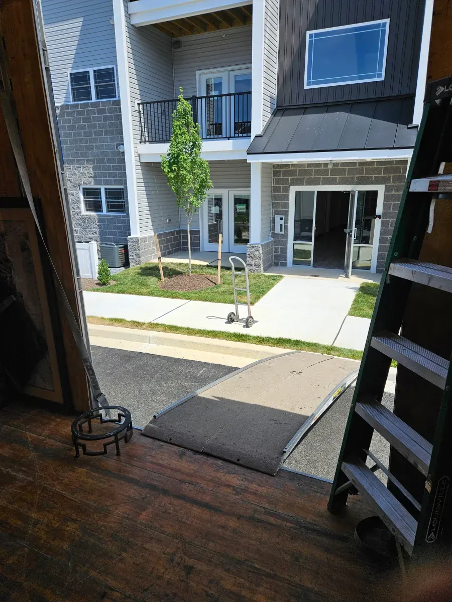View from inside a moving truck, loading ramp down to sidewalk and apartment building entrance.