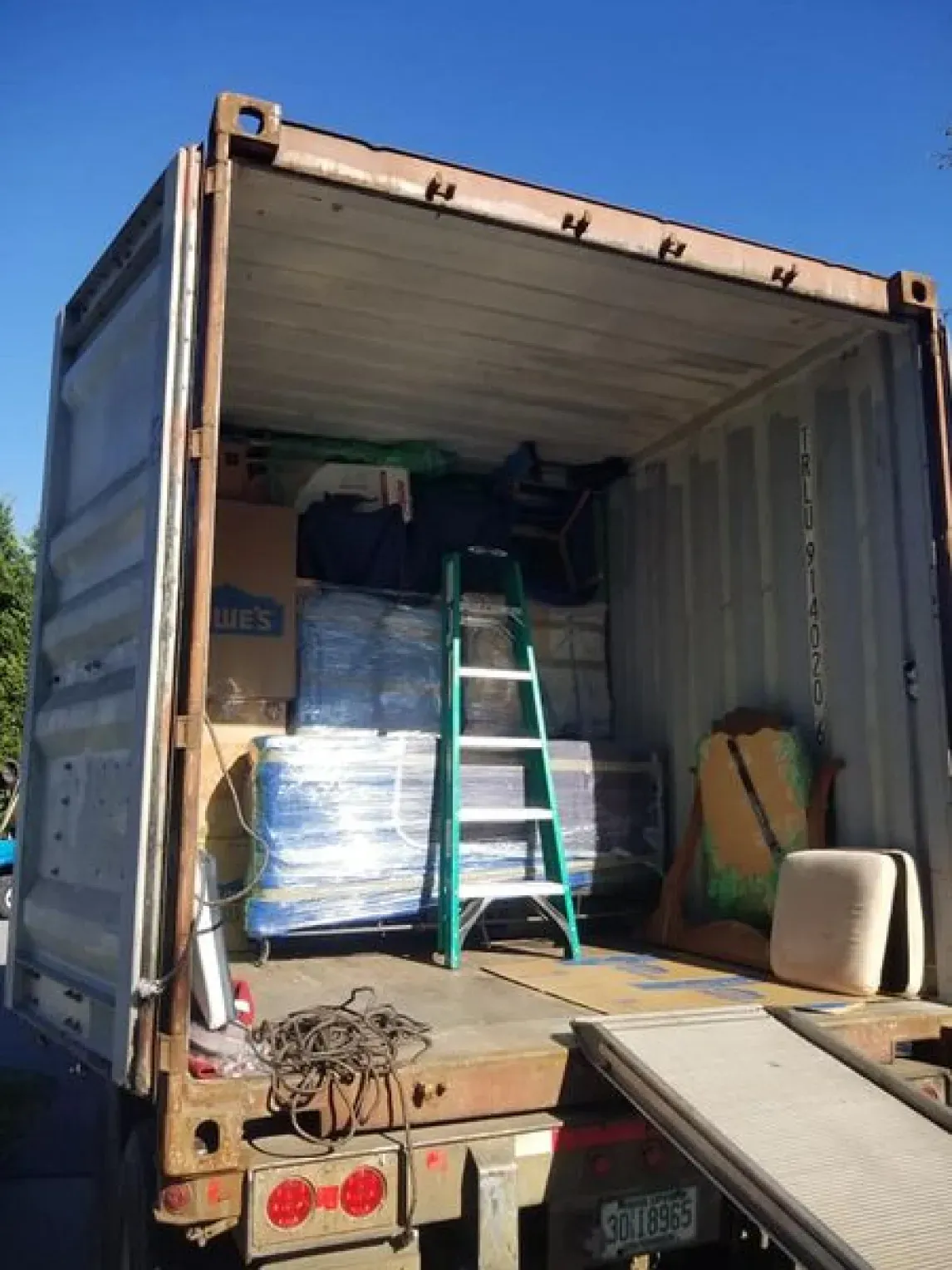 Open container truck loaded with furniture, boxes, and a ladder.