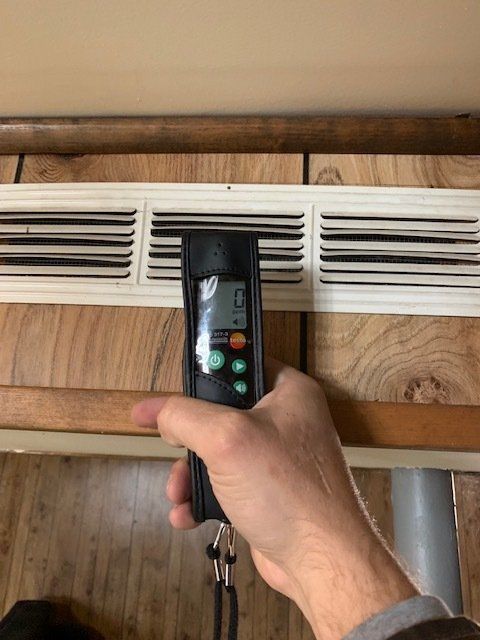 A person is holding a remote control in front of a vent.