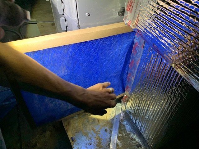 A person is working on a piece of metal with a blue tarp in the background.