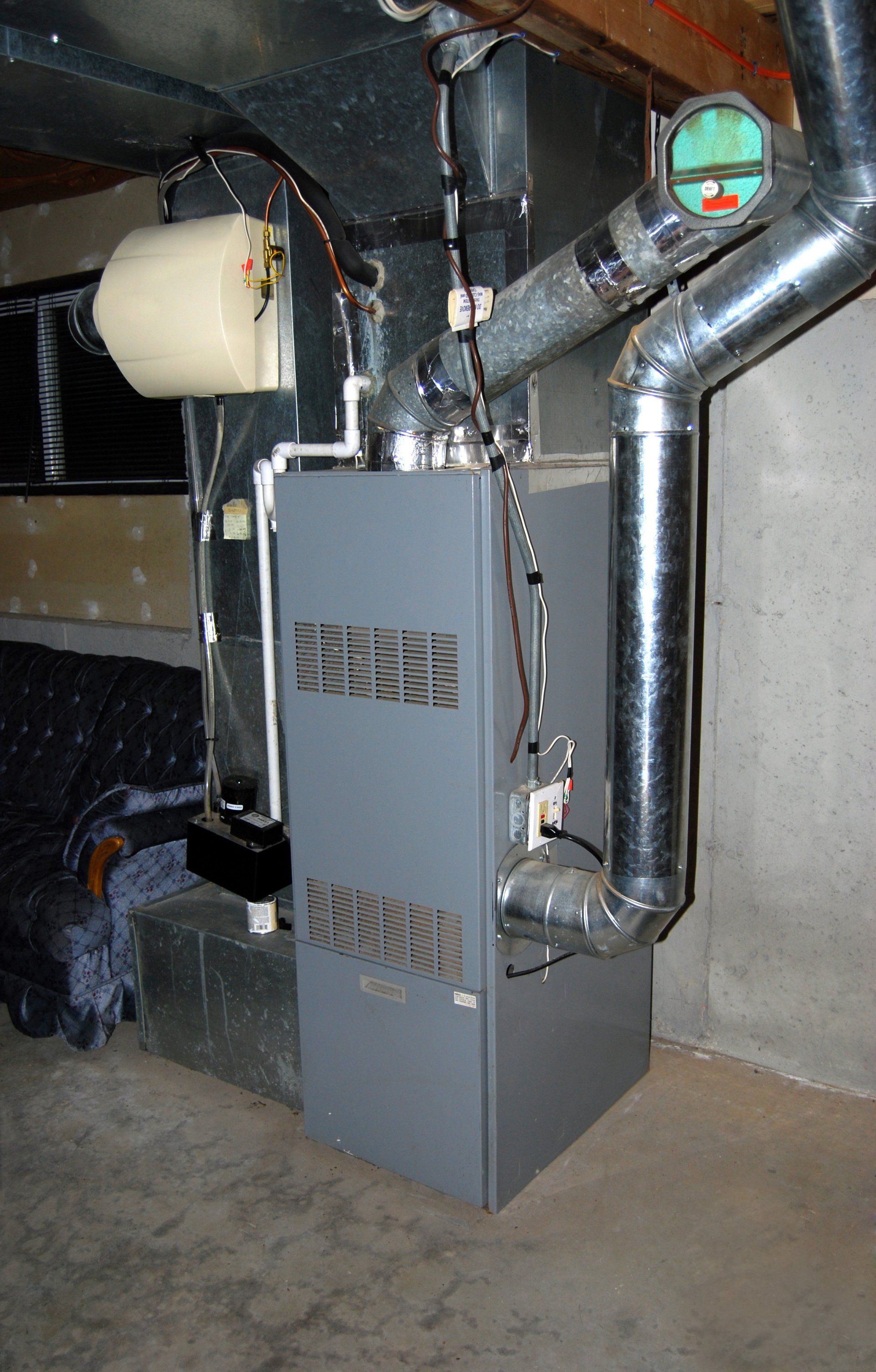An air conditioner is sitting in a basement next to a couch.