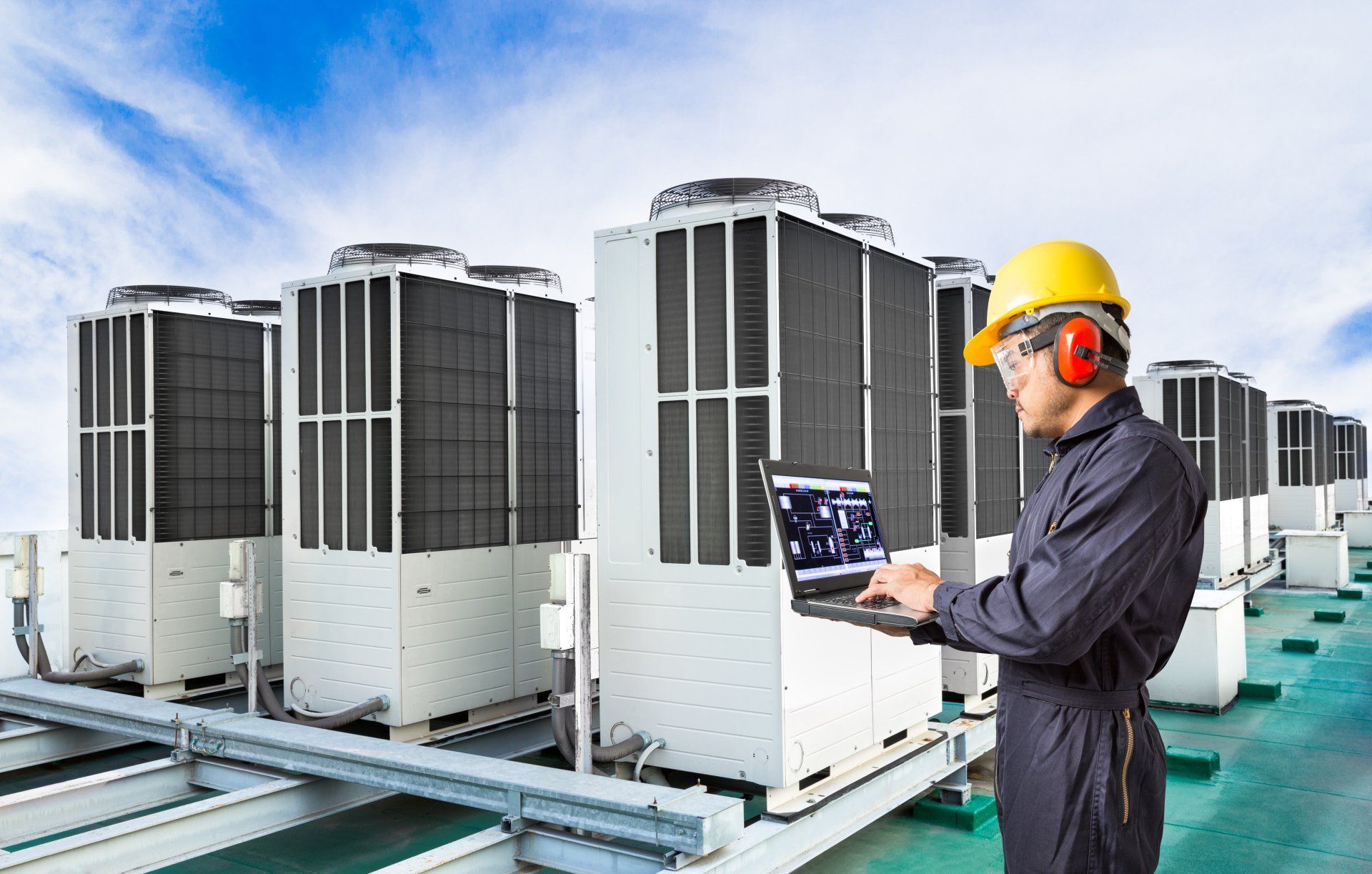 A man is using a laptop computer in front of a row of air conditioners.