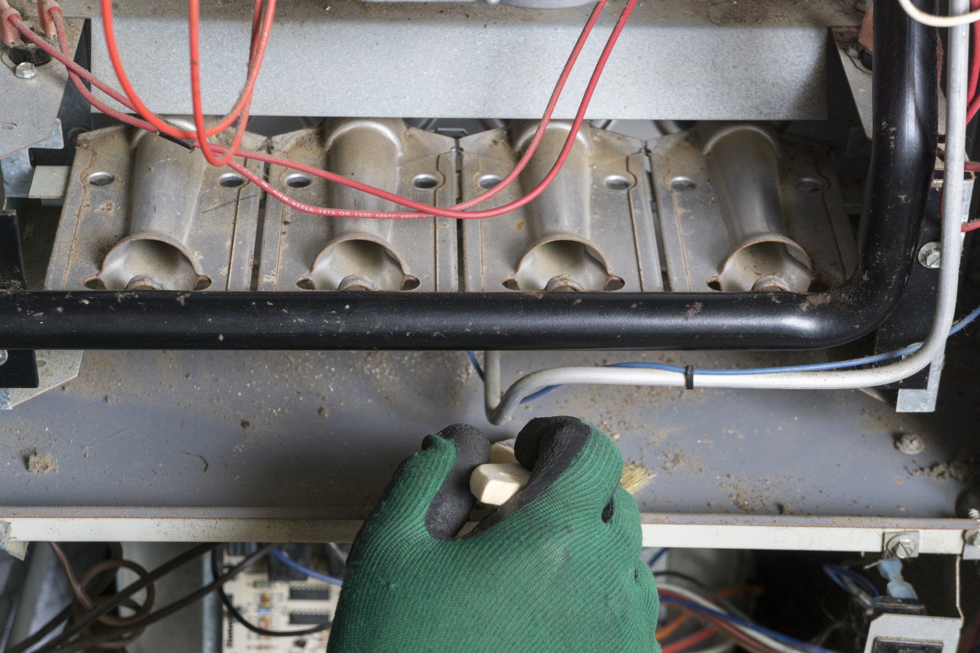 A person wearing a green glove is working on a heater.