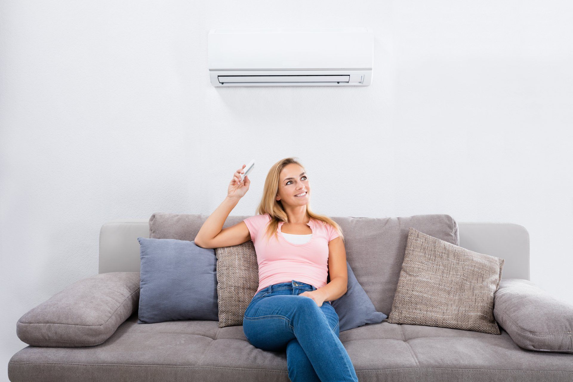 A woman is sitting on a couch in front of an air conditioner.